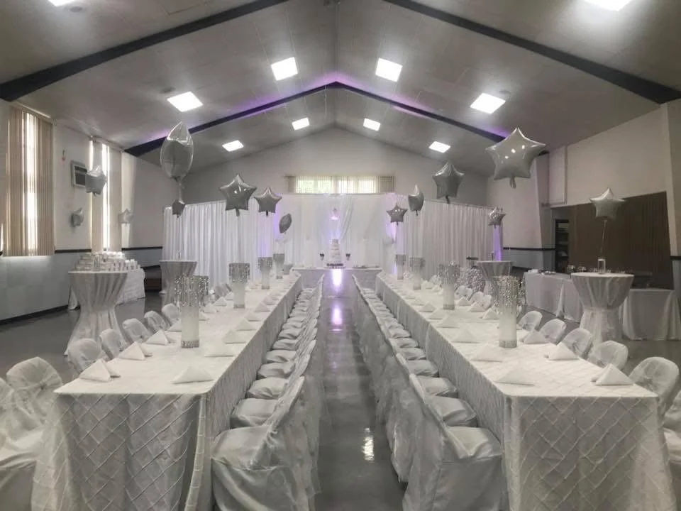 Indoor event hall decorated with white drapery, star-shaped balloons, and elegant table settings for a celebration.