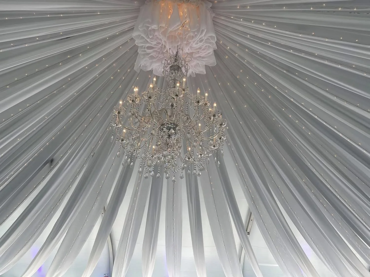 White draped ceiling with small string lights and a large ornate chandelier.