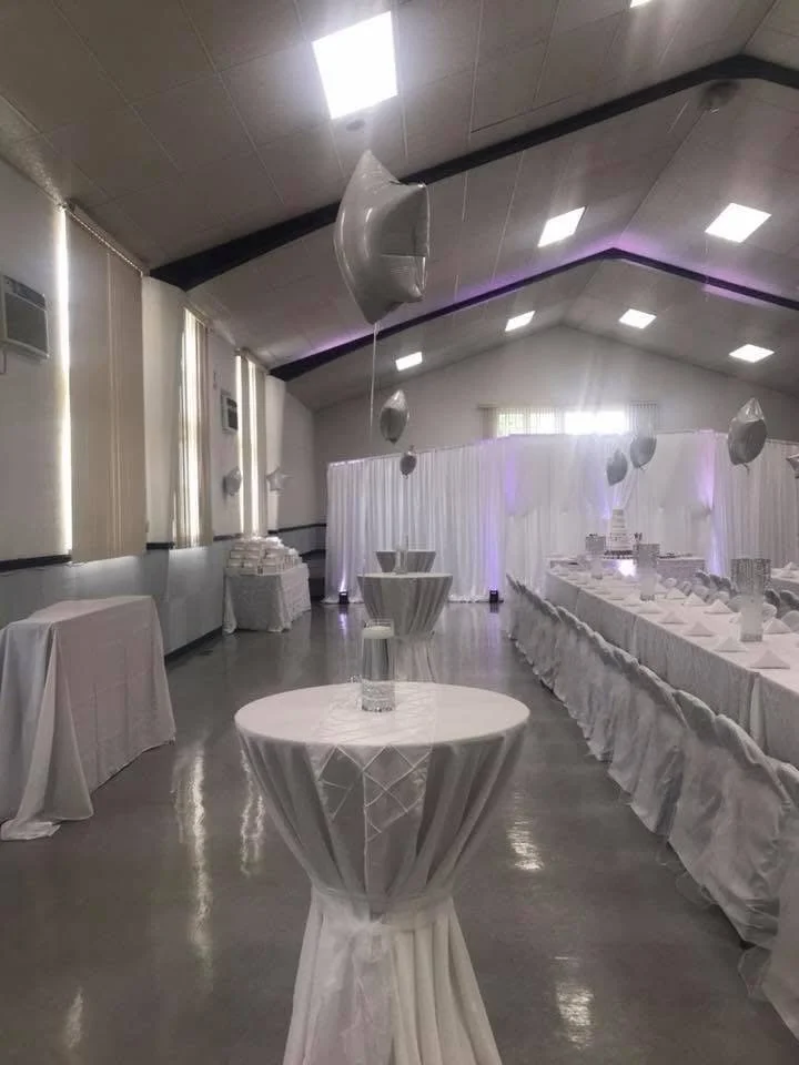 A decorated banquet hall with white tablecloths, hanging balloons, and draped curtains for a celebration or event.