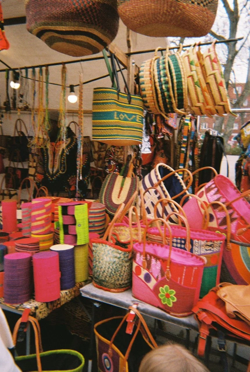 Colorful woven bags and hats displayed at an outdoor market stall.