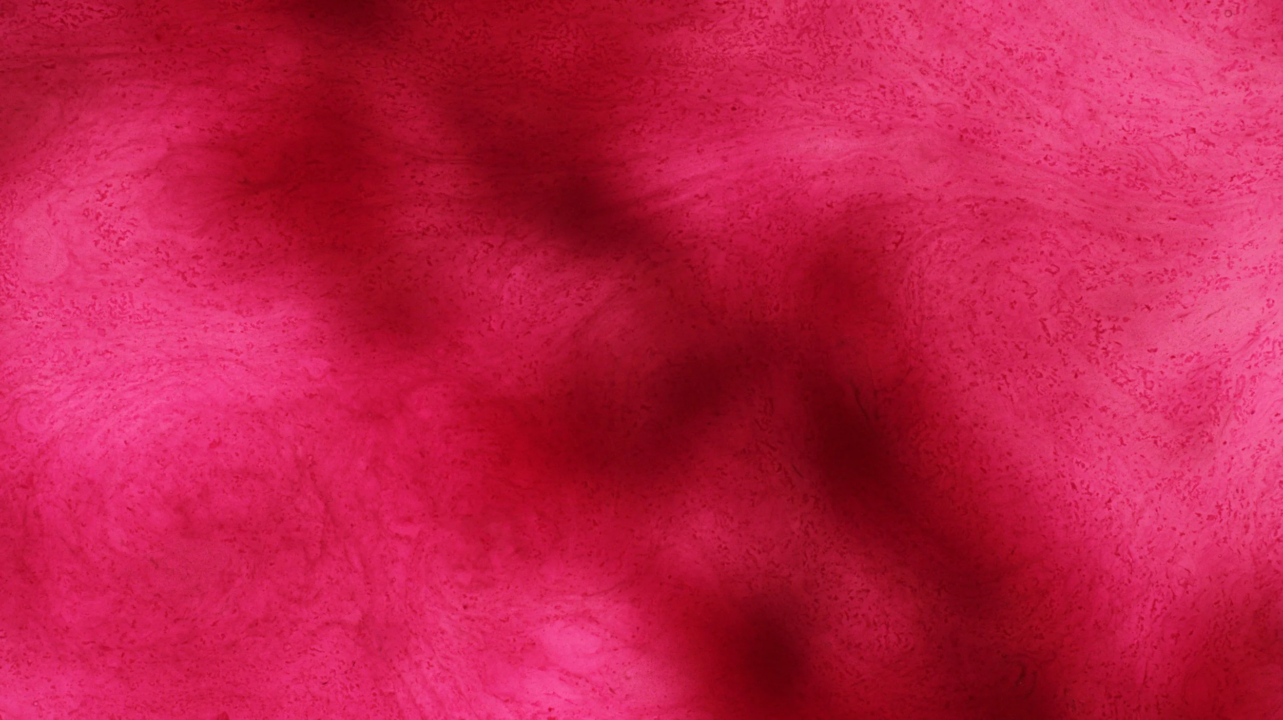 Close-up of a pink textured surface with darker shadows and variations in color.