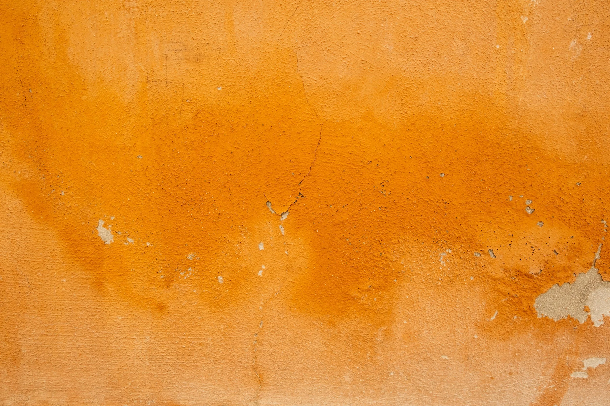 Close-up of a weathered orange wall with peeling paint and cracks.