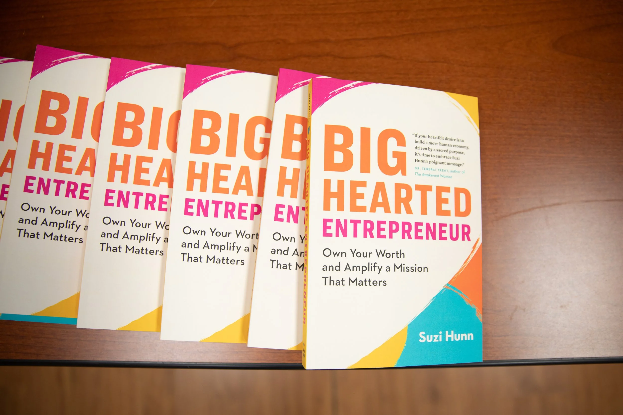 Multiple copies of a book titled 'Big Hearted Entrepreneur' by Suzi Hunn arranged on a wooden surface, with one copy slightly angled.