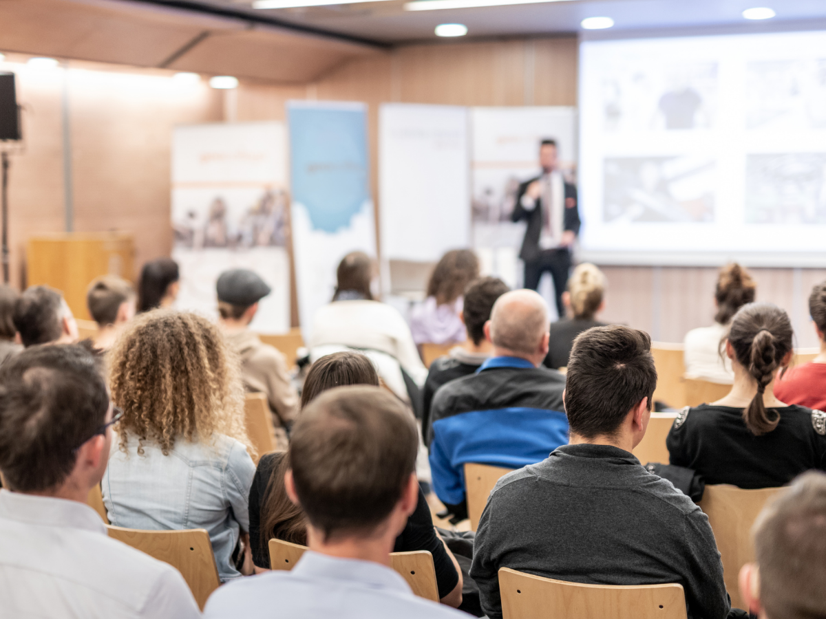Audience attending a presentation in a conference room with a speaker at the front