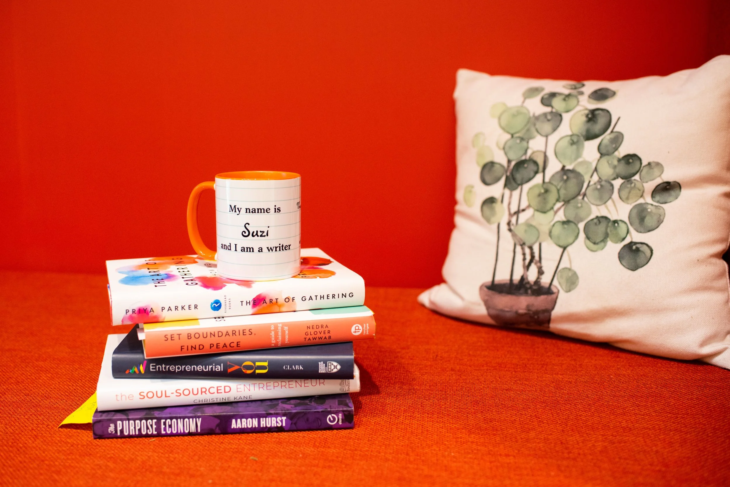 A stack of books on entrepreneurship is topped by a mug that says, "My name is Suzi and I am a writer."