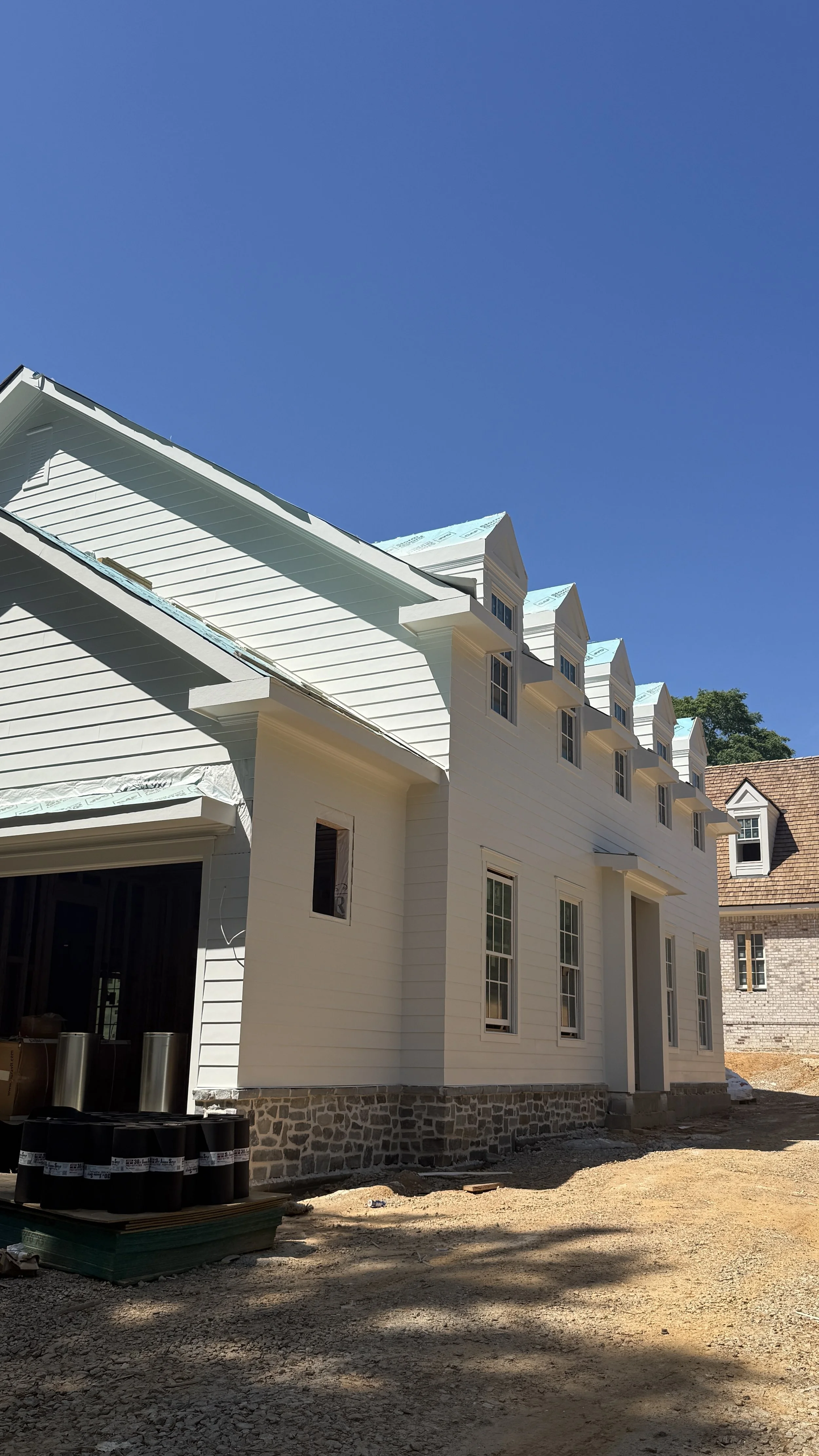 Newly constructed white home with large windows, stone foundation, and front yard materials showcasing modern custom home design.