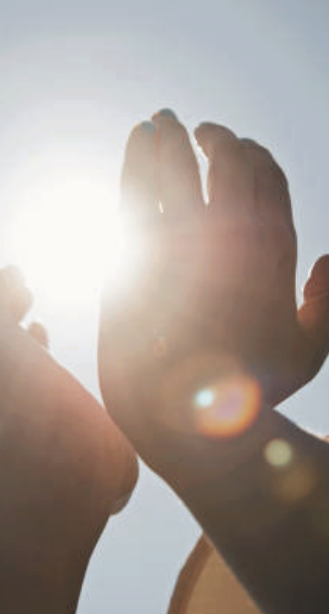 A person's hand reaching towards the sun with sunlight shining through fingers, creating sun flare.