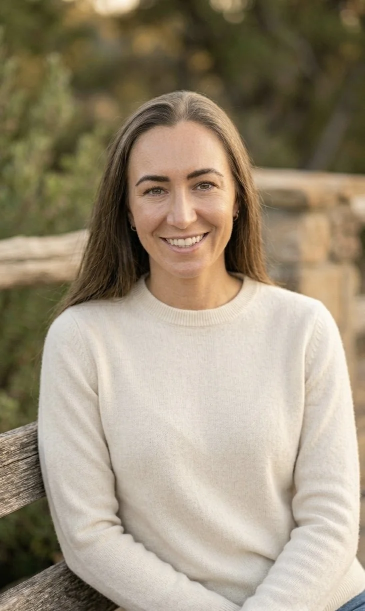 Dark brown haired Woman sitting outside on bench smiling at the camera