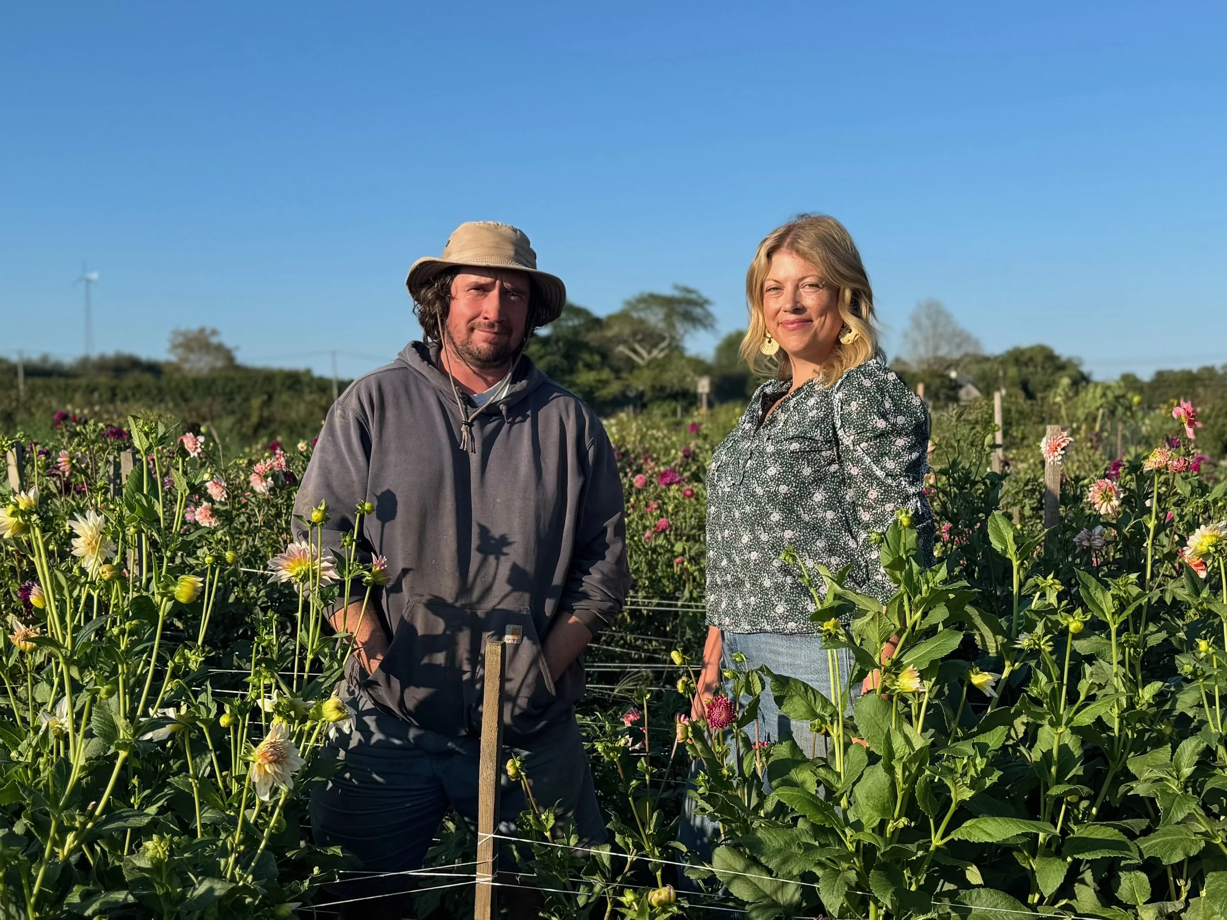 A man and woman standing in a flower field on a clear, sunny day.