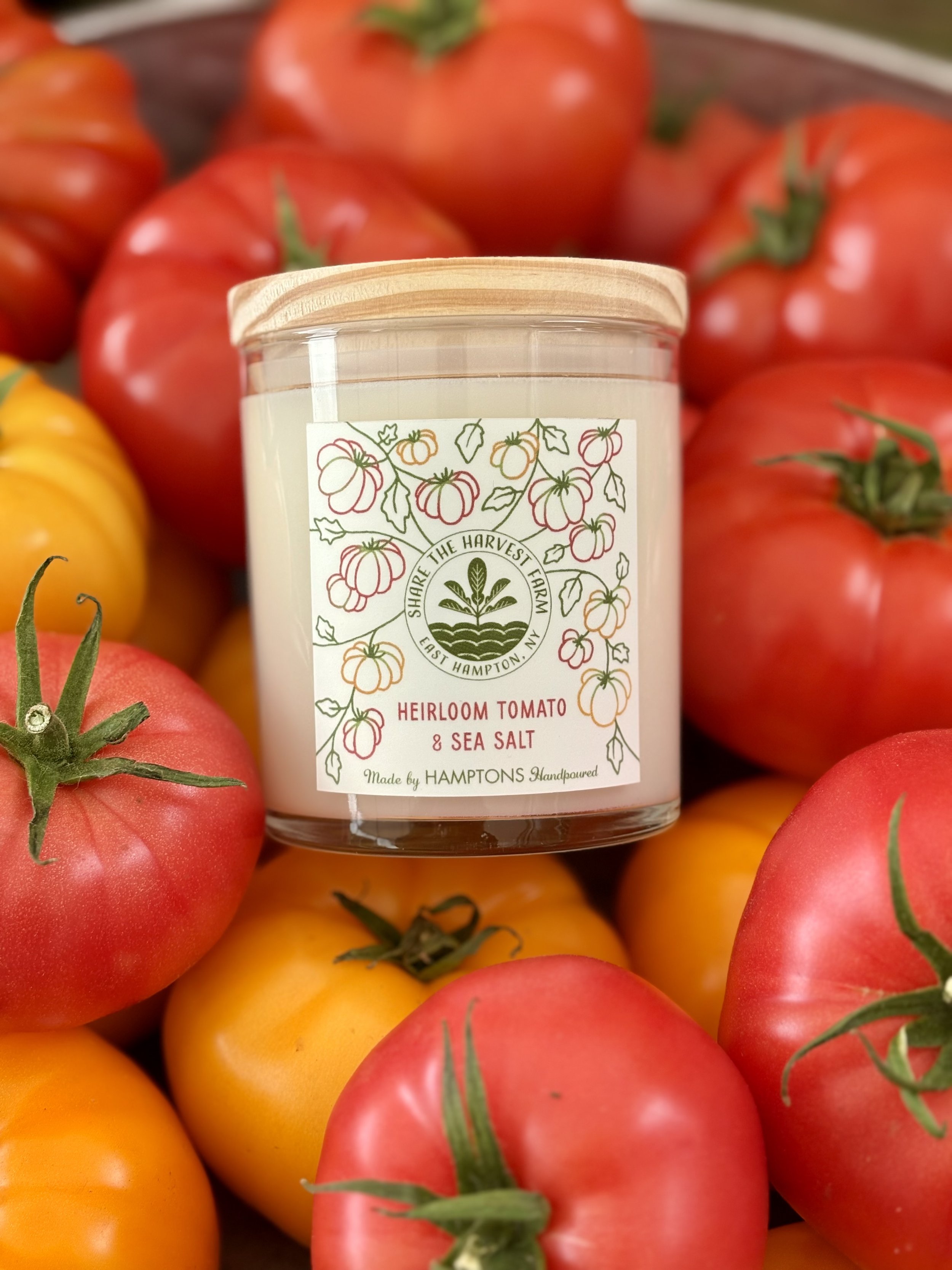 A candle with a label that features illustrations of tomatoes and vines, surrounded by red and yellow tomatoes.