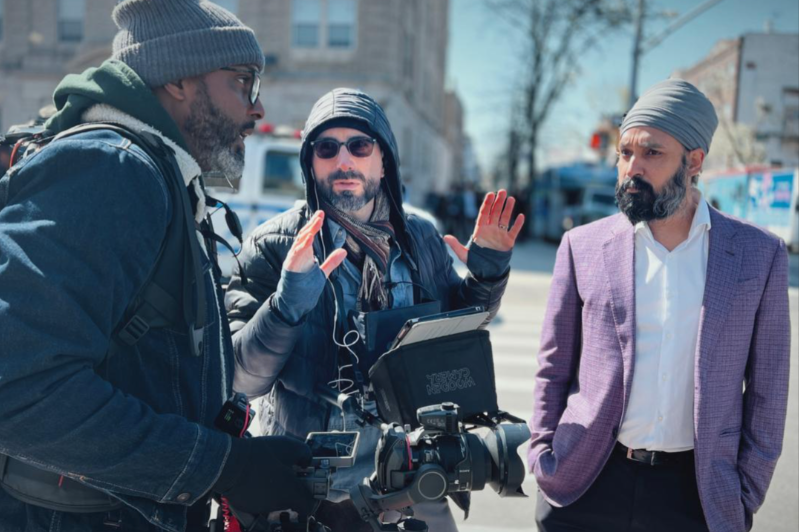 Filmmakers Jack Gordon and Damel Dieng from the documentary production company Digital Development Communications with religion scholar Simran Jeet Singh having a conversation on a New York City street, with one man gesturing with his hands.