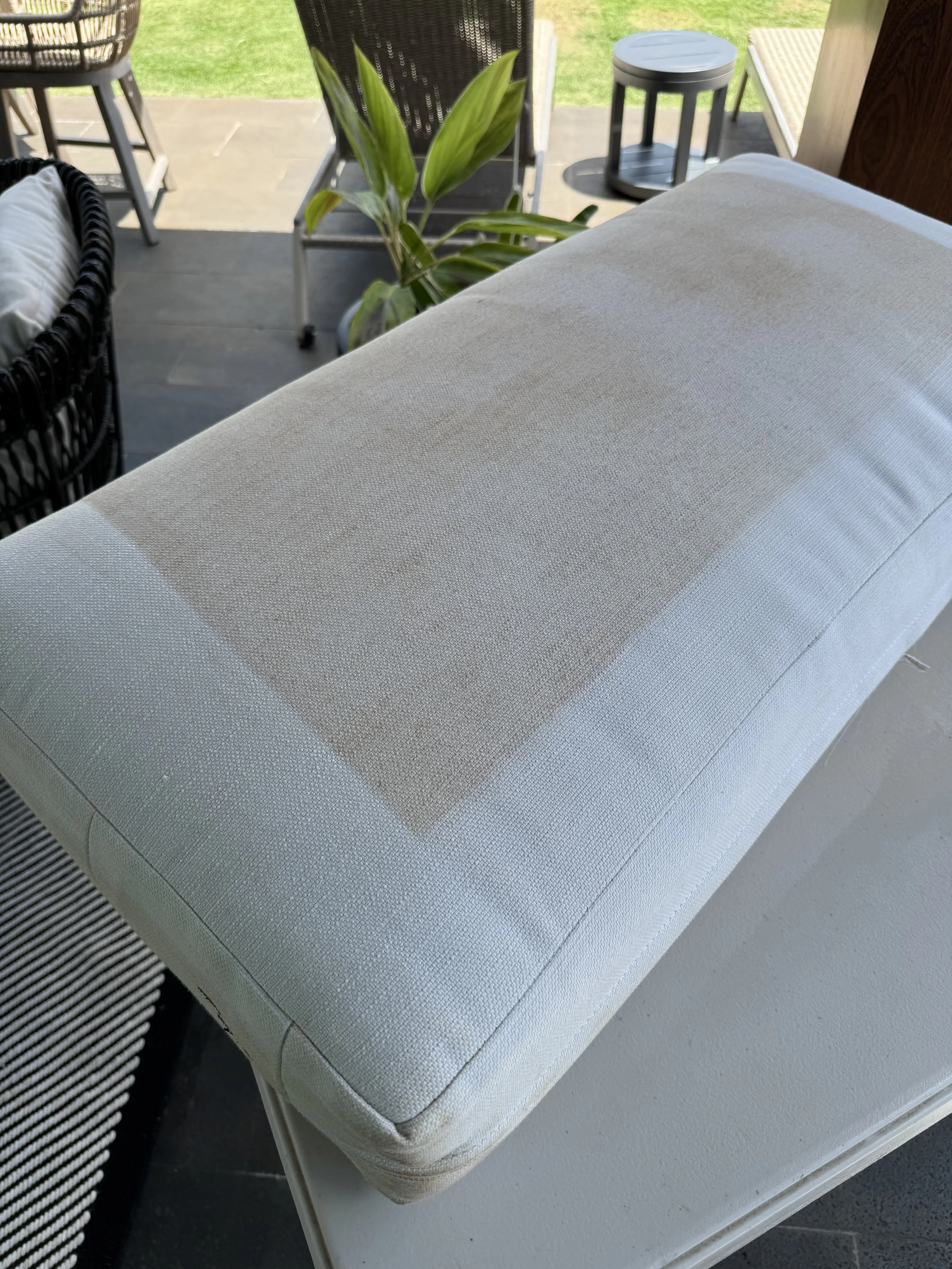 Close-up of a light-colored upholstered outdoor lounge chair with a large stain or dirt mark on the cushion.