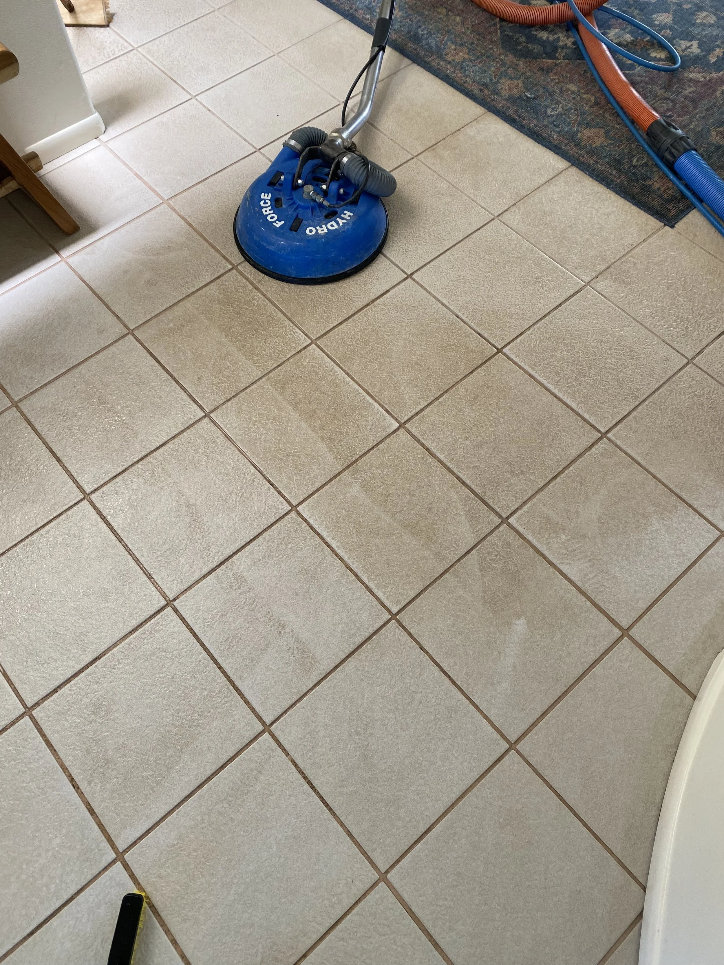 Cleaning floor with a blue floor buffer in a tiled room, with cleaning equipment visible.