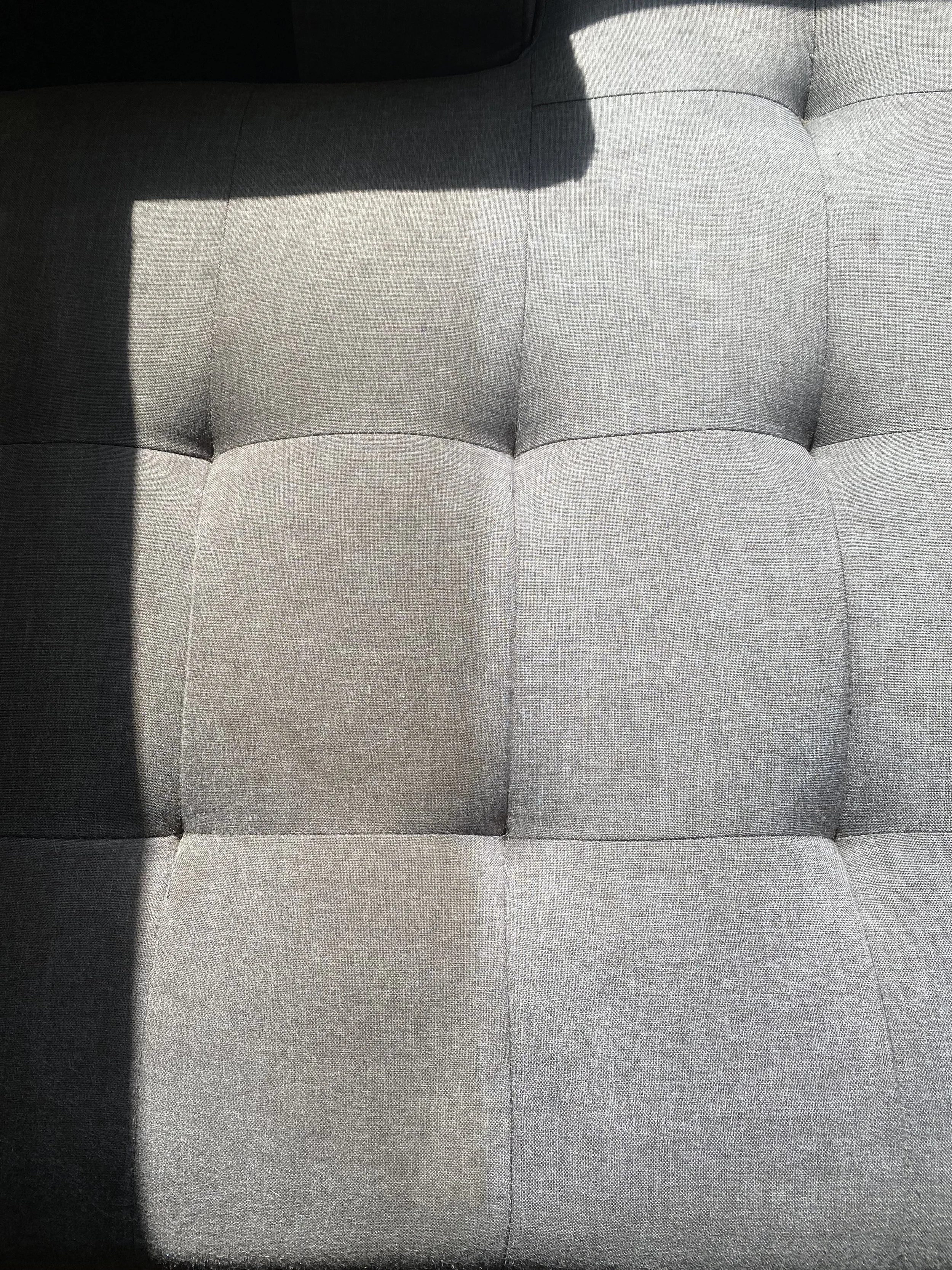 Close-up of a gray tufted fabric chair with a shadow cast on it.