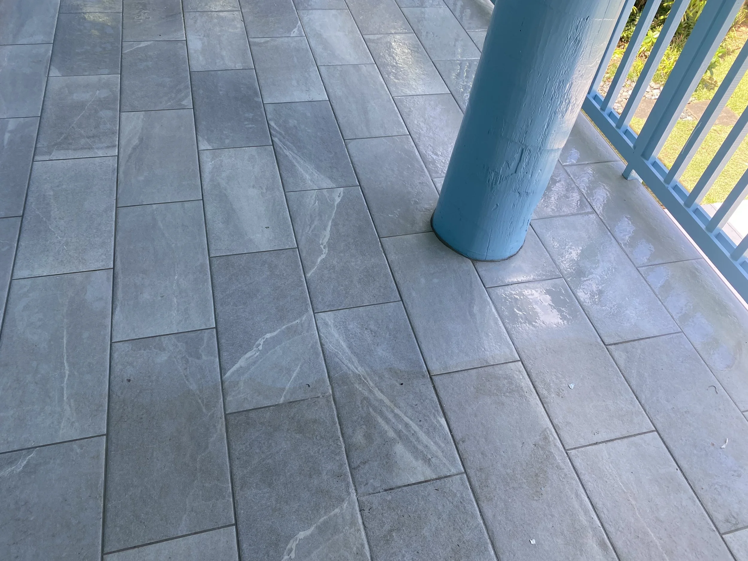 Gray outdoor tiles, a blue metal post, and a blue railing in the background.