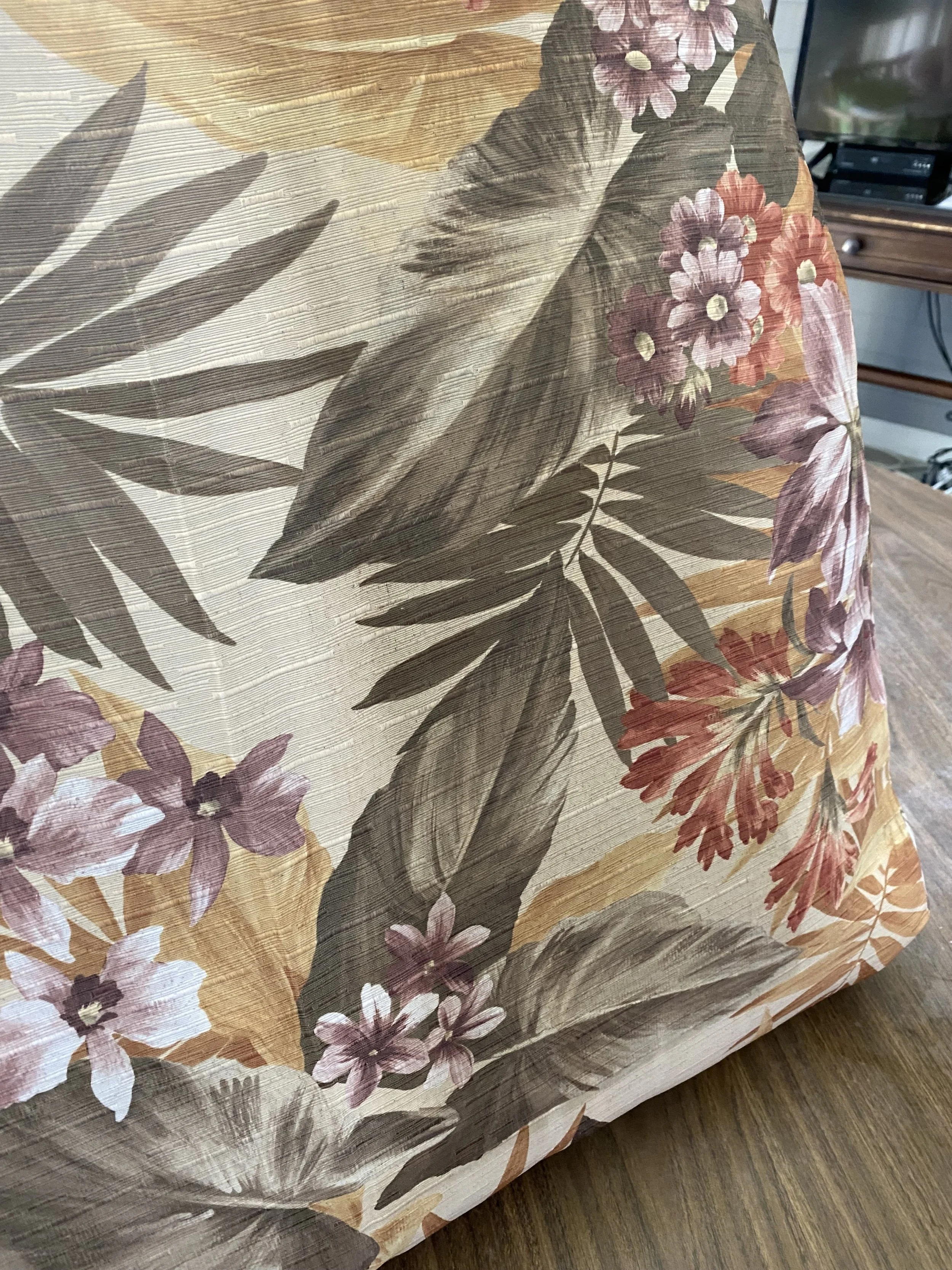 A close-up of a floral patterned fabric with large leaves and various colorful flowers in shades of pink, purple, and red, draped over a wooden surface.