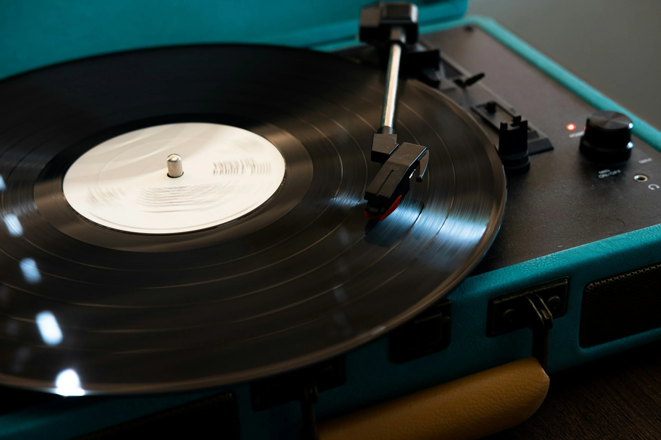 Close-up of a vintage turntable playing a vinyl record with a white label, set on a blue and black portable player.