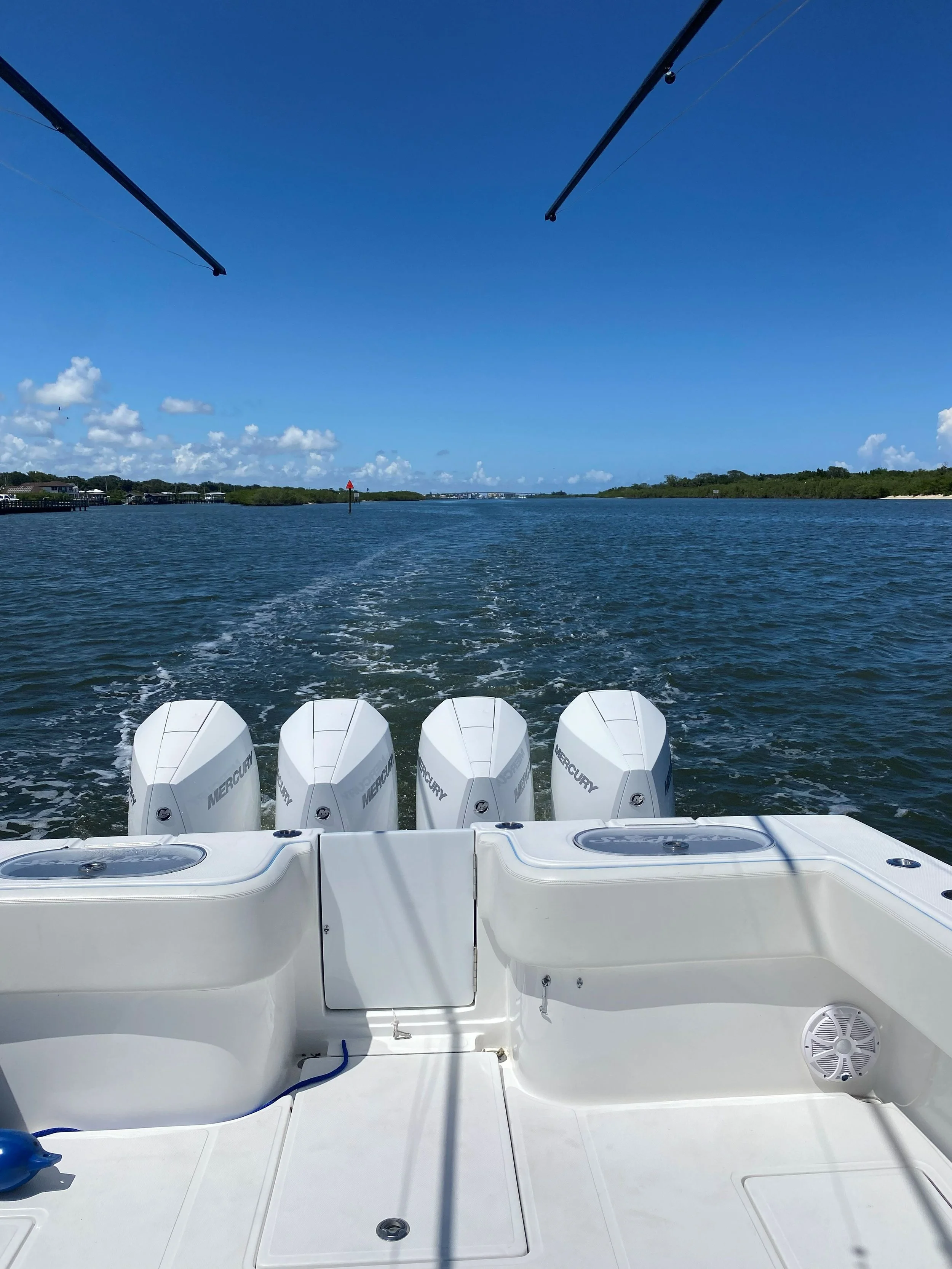 View from a boat showing water and sky with four Mercury outboard motors, part of the boat's stern, and a wake trail in the water.