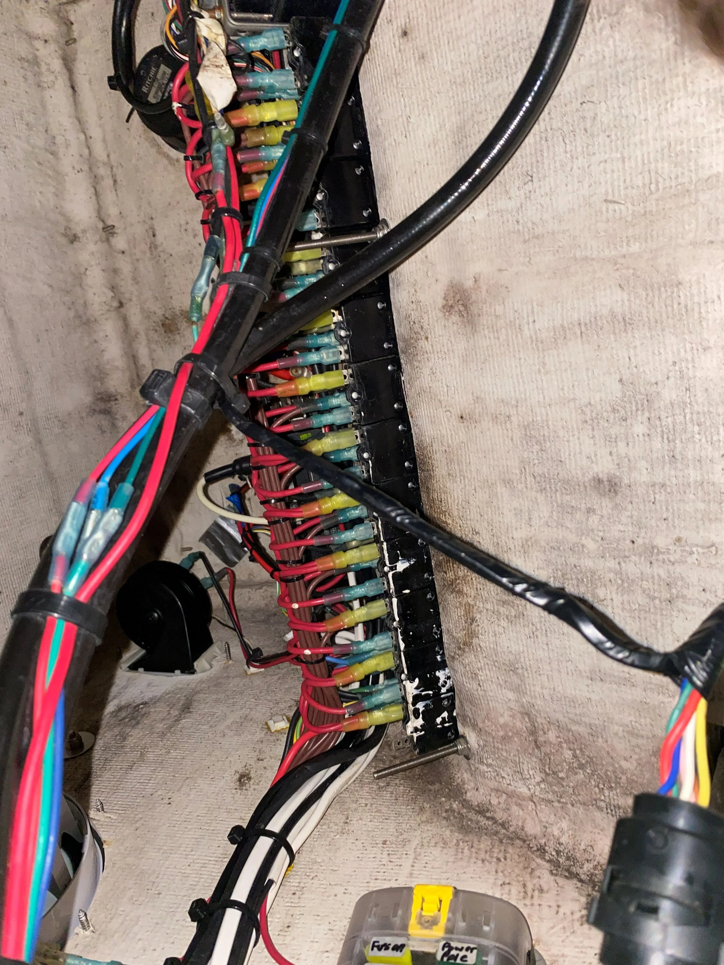 Electrical wiring and components mounted on a black panel attached to a concrete wall.