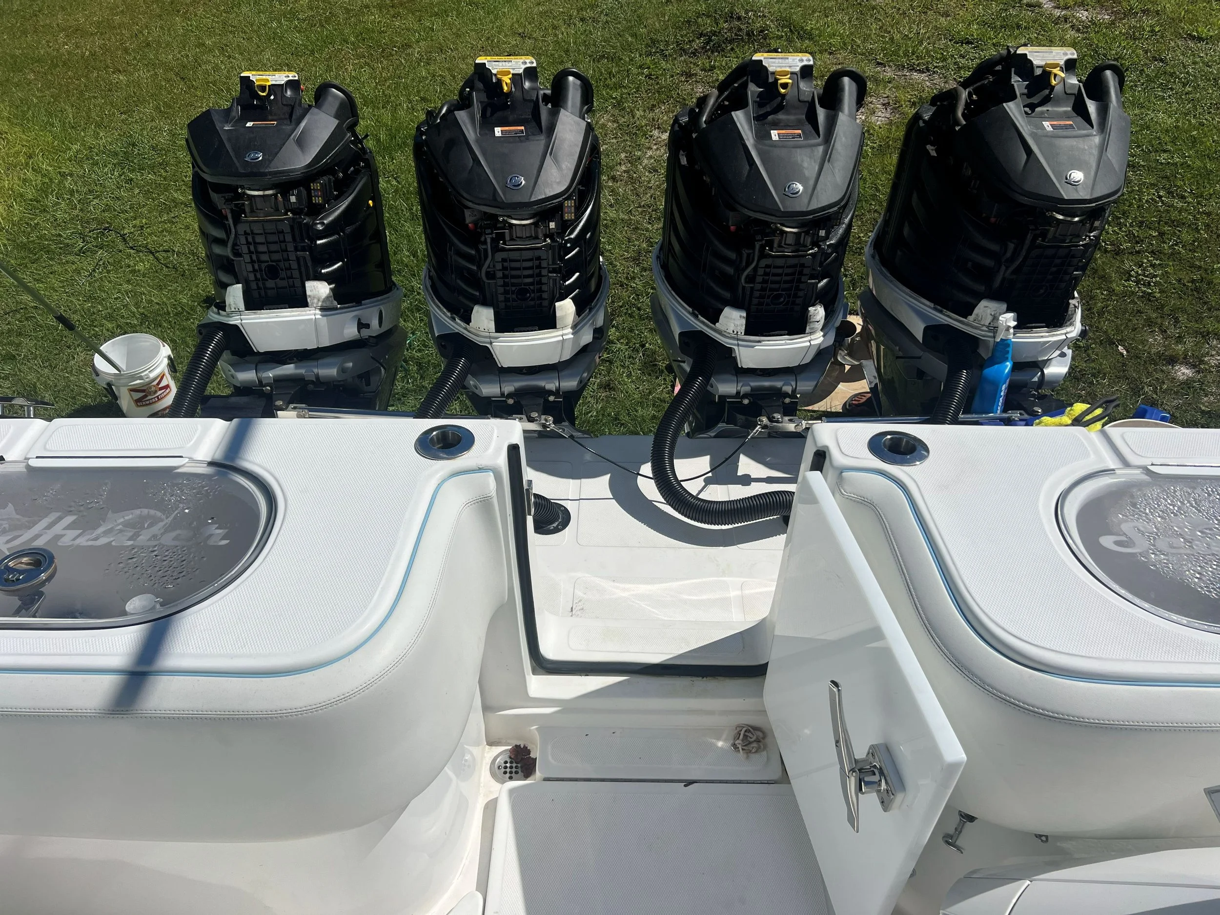 Four outboard boat engines mounted on a white boat deck, with a grassy area in the background.