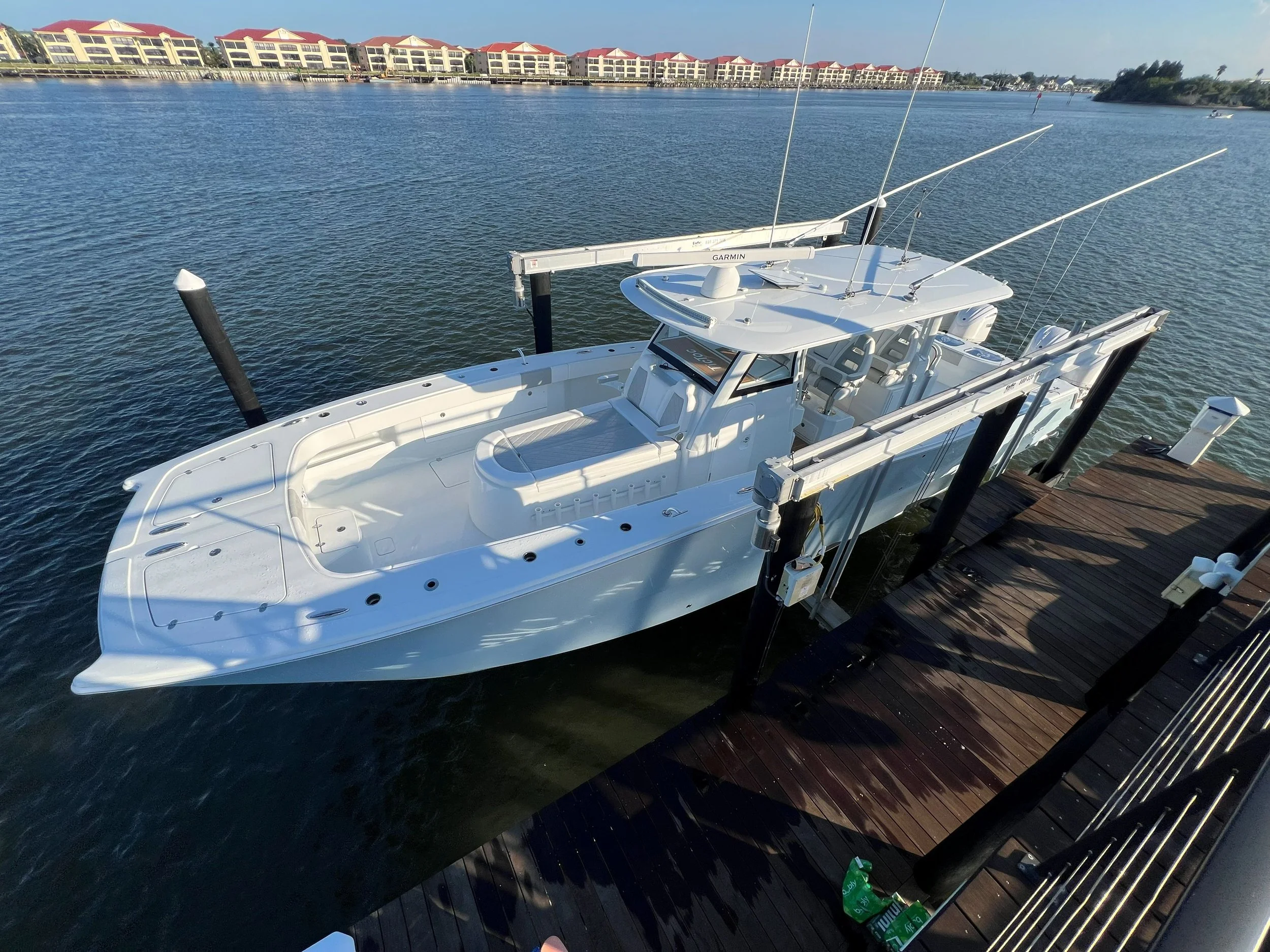 A white yacht docked at a wooden pier on a calm body of water, with a row of colorful buildings in the background under a clear blue sky.
