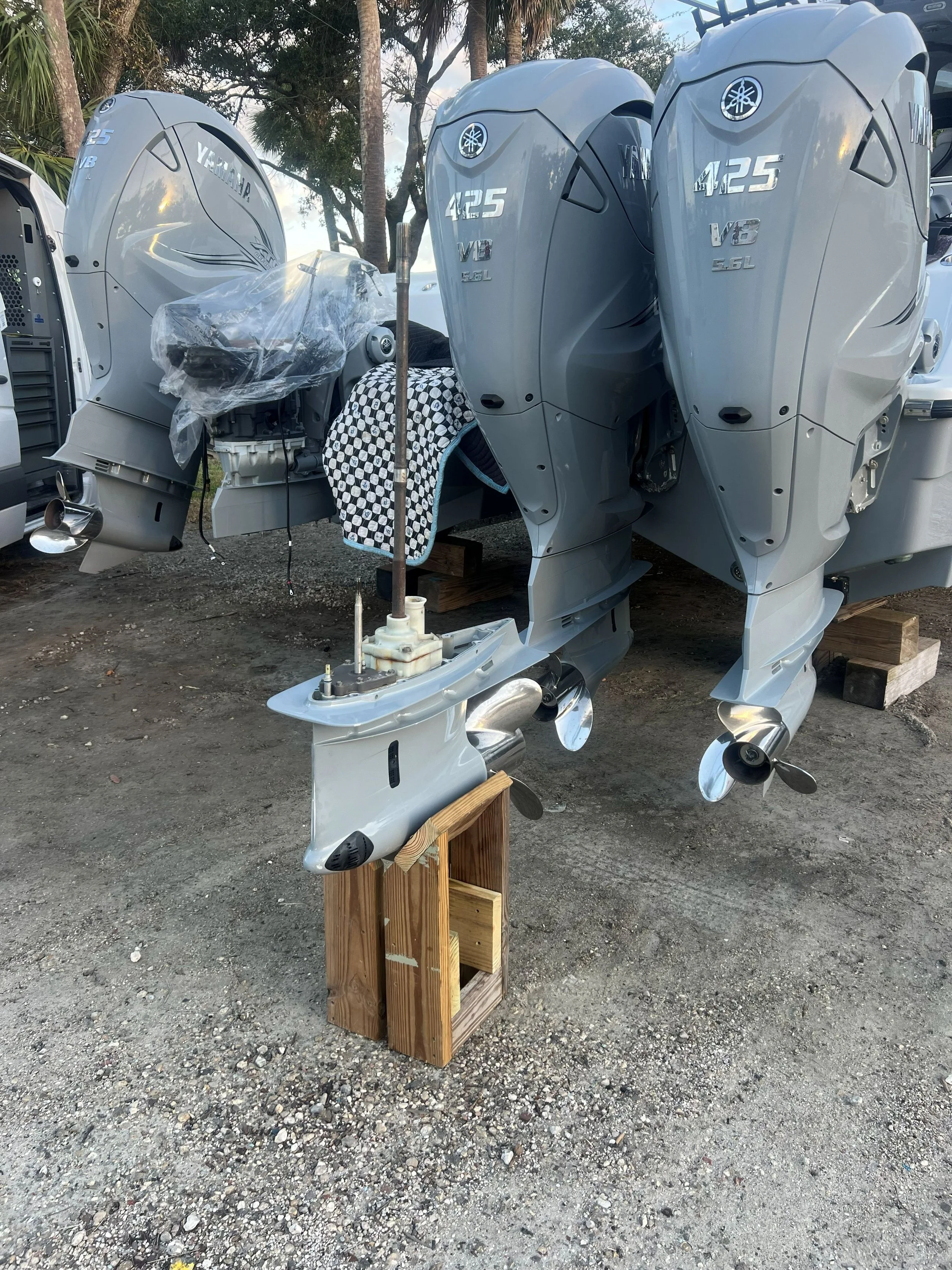 Three Yamaha outboard motors with silver covers mounted on a wooden stand outdoors, with trees in the background.