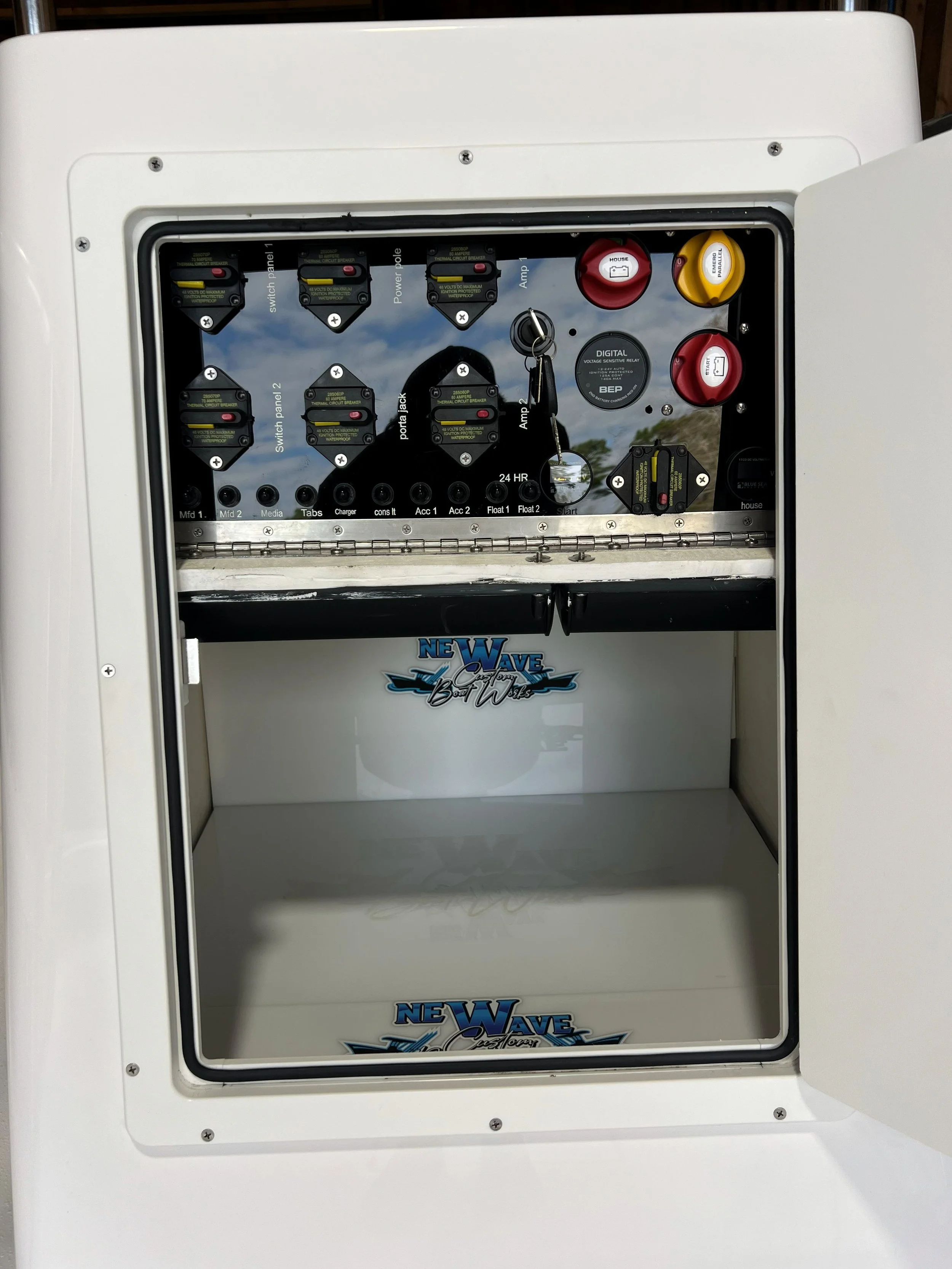 Open electrical panel with switches, fuses, and labels, and a storage compartment with a 'New Wave' logo.