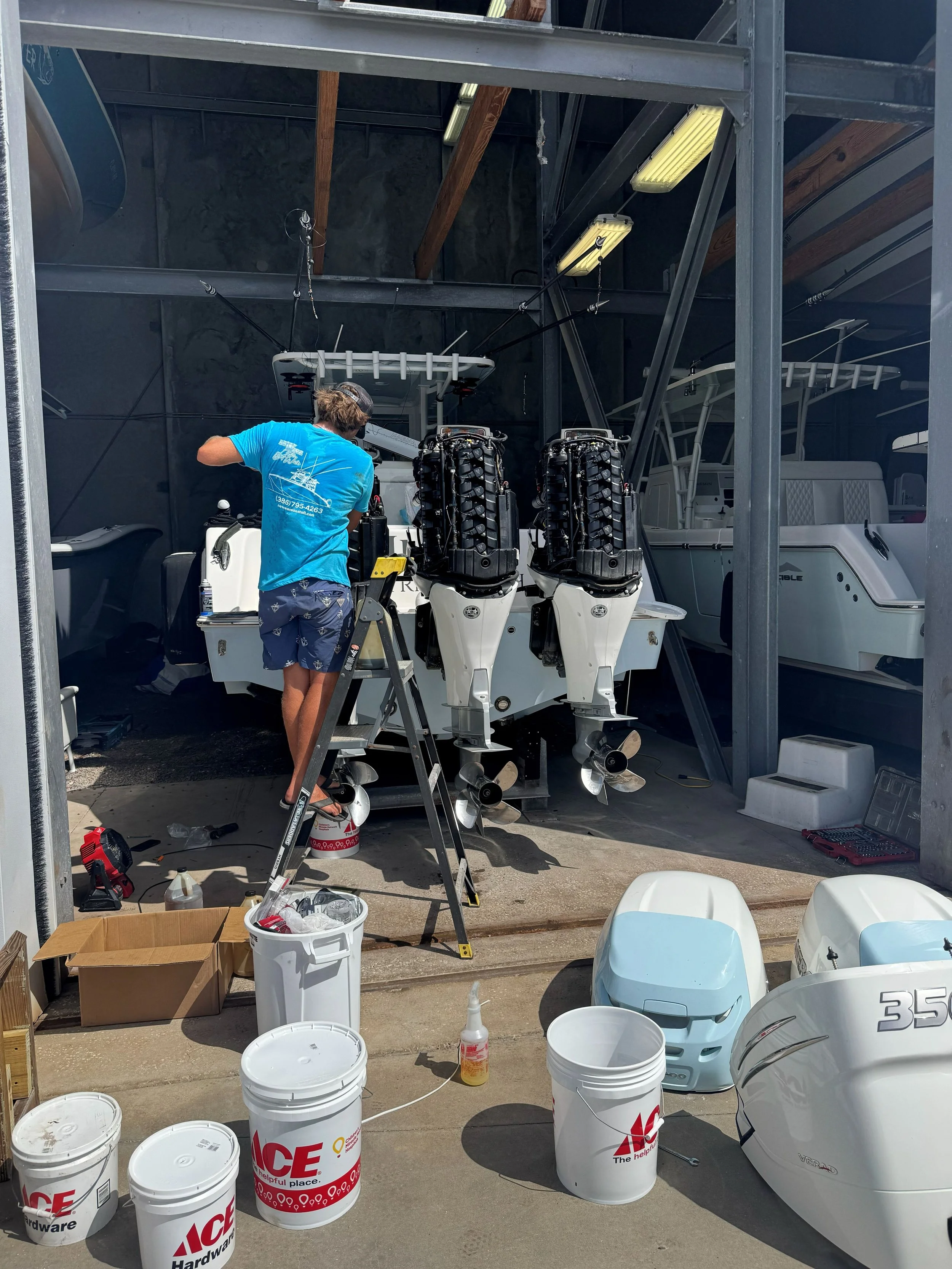 Person working on boat motors in a garage or workshop surrounded by tools, buckets, and boat parts.