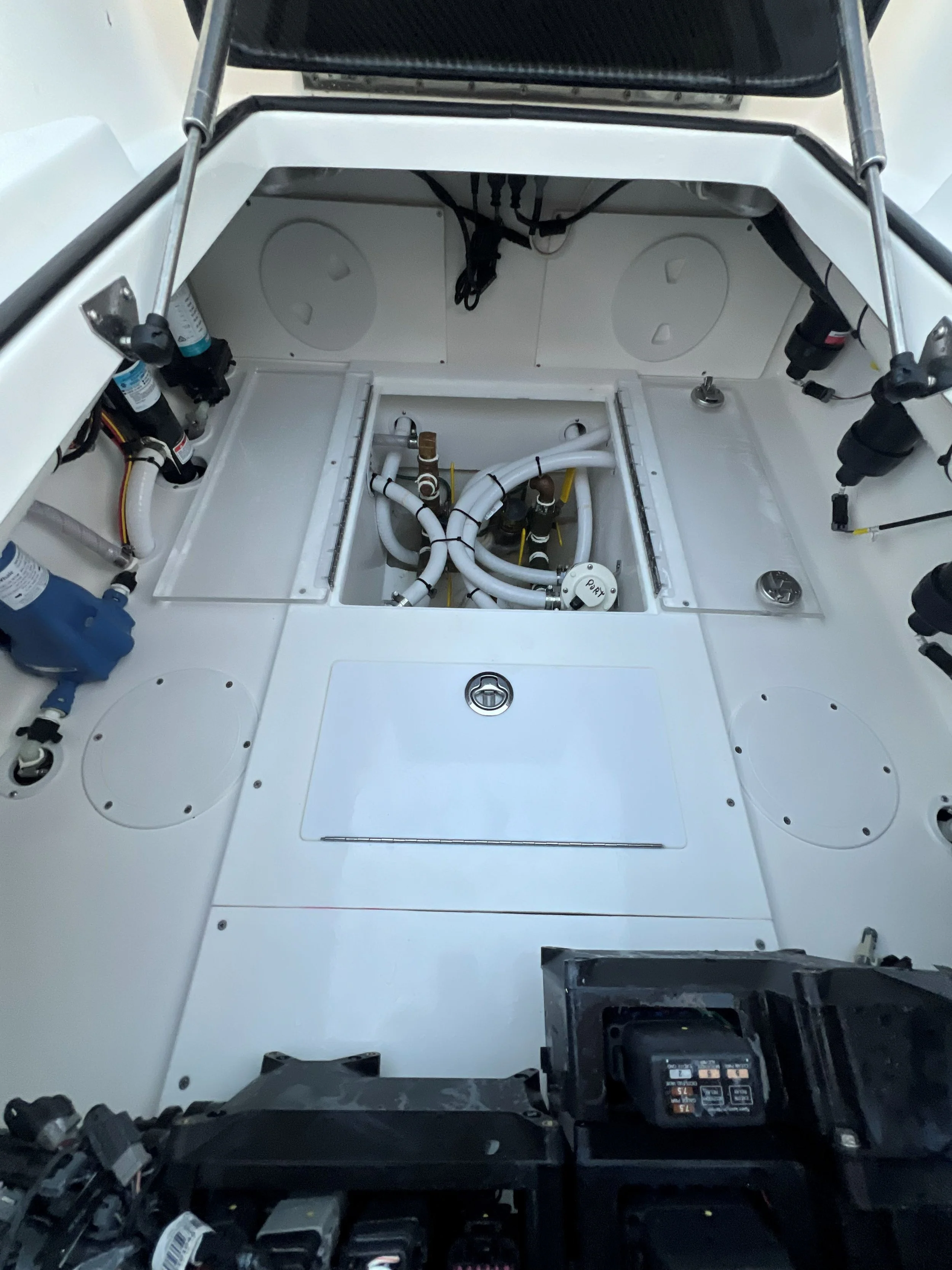 Interior of a boat's engine compartment with white panels, plumbing, hoses, and electrical components.