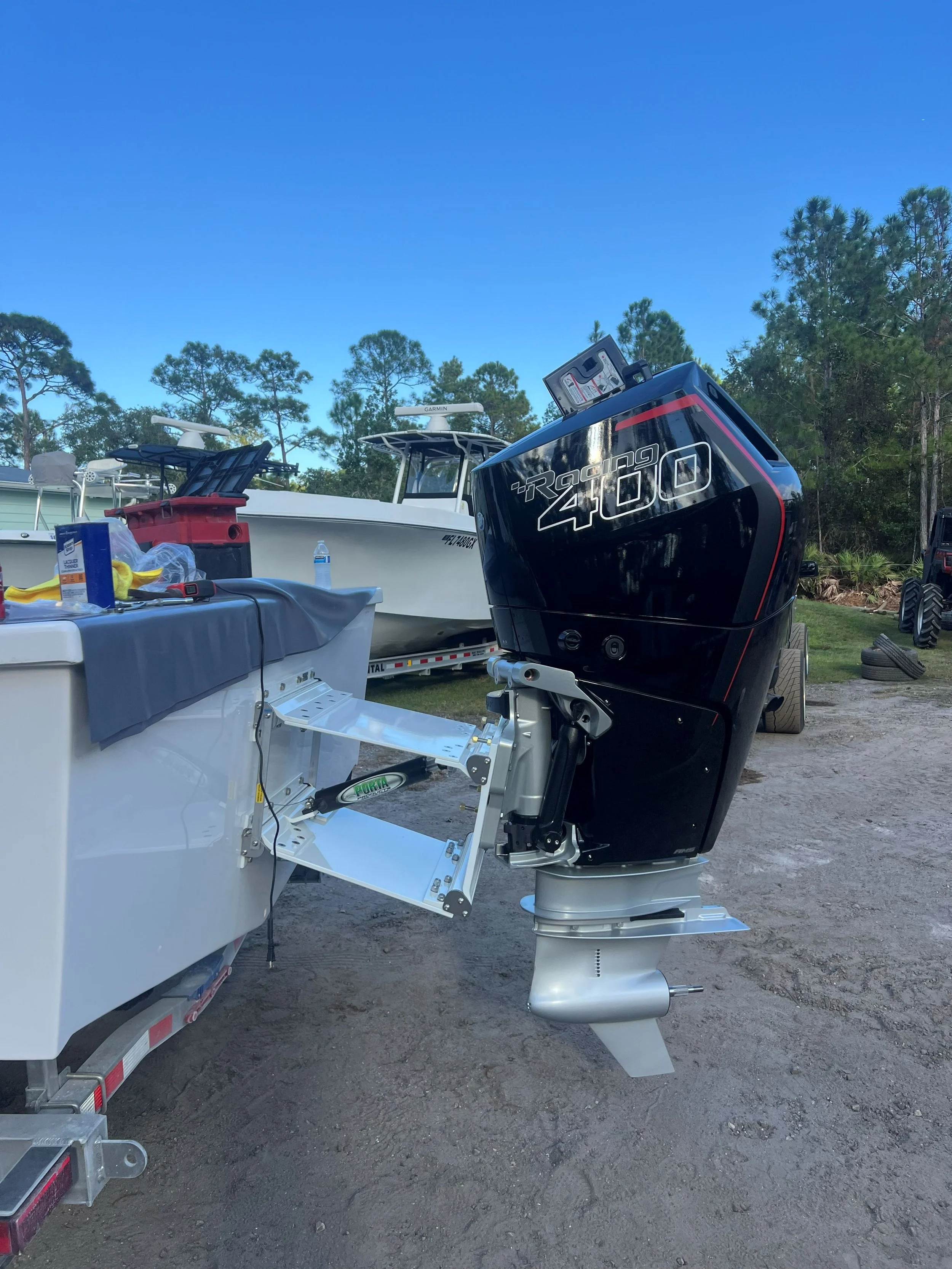 A black racing 400 outboard motor attached to a white boat on a trailer, with other boats and trees in the background.