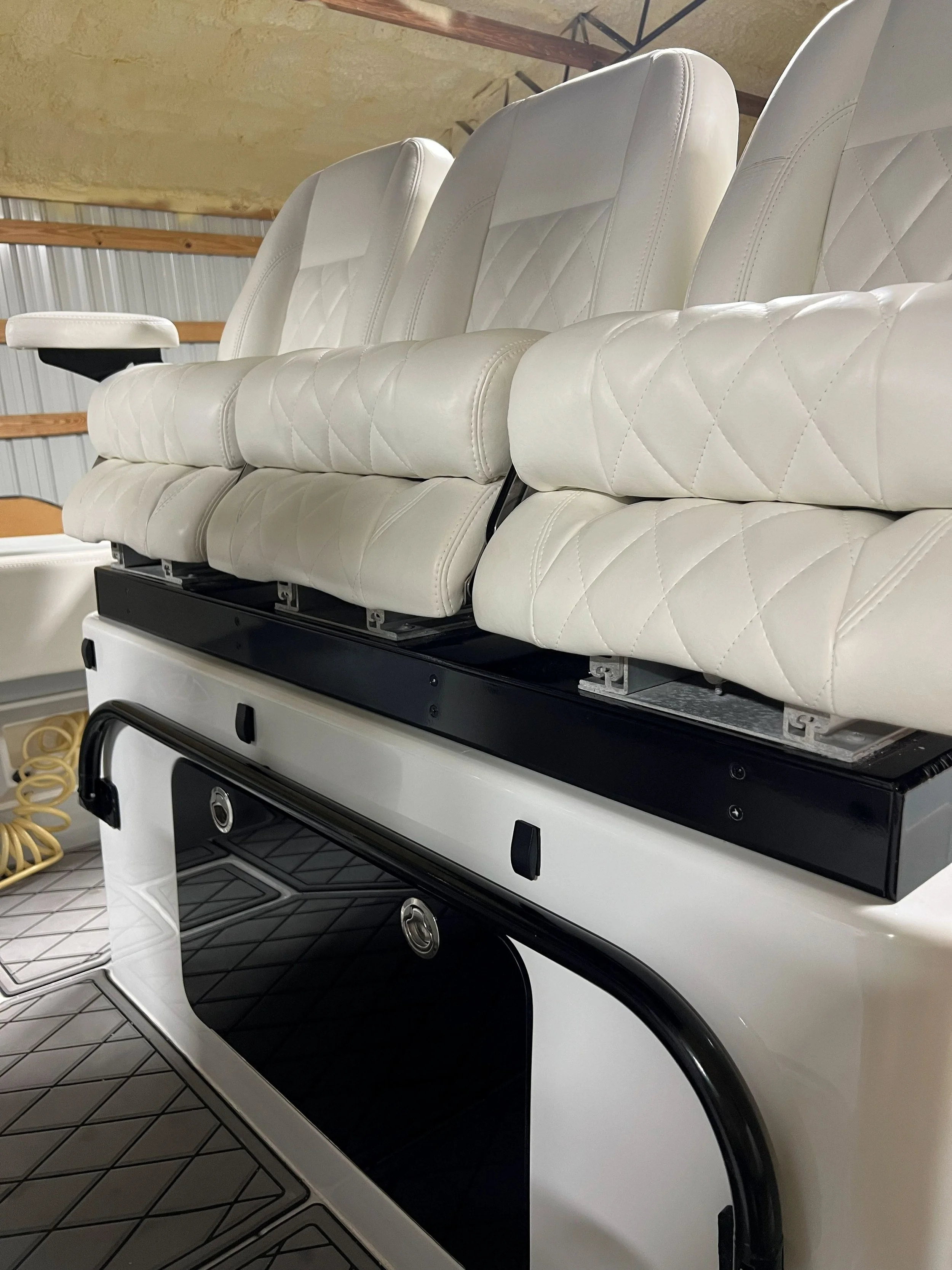 Close-up of white boat seats with diamond stitching, mounted on a black and white boat interior.
