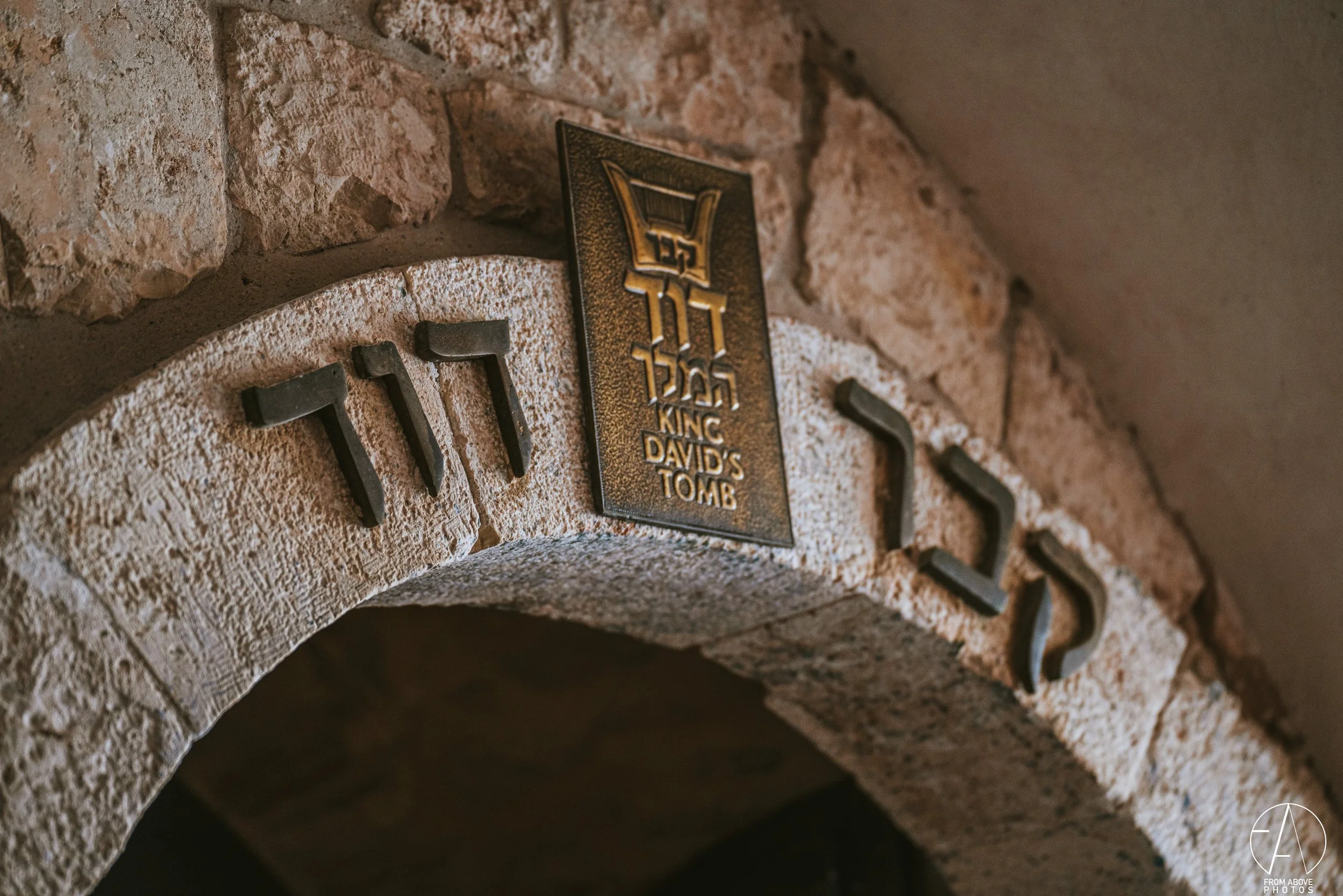 Close-up of a stone archway with the words 'KING DAVID'S TOMB' on a plaque and the Hebrew letter Shin on the stones.