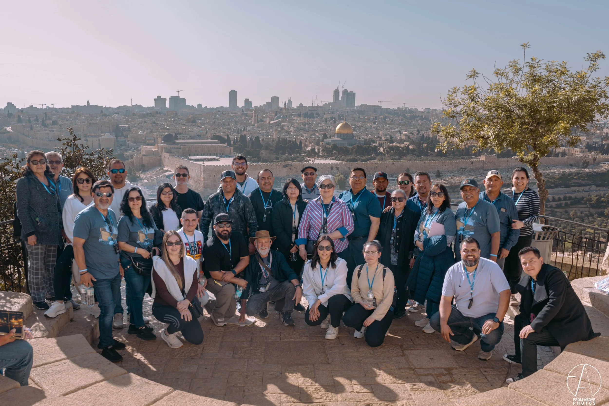 Group of people posing for a photo on a hill with a city skyline and dome in the background, sunny day.