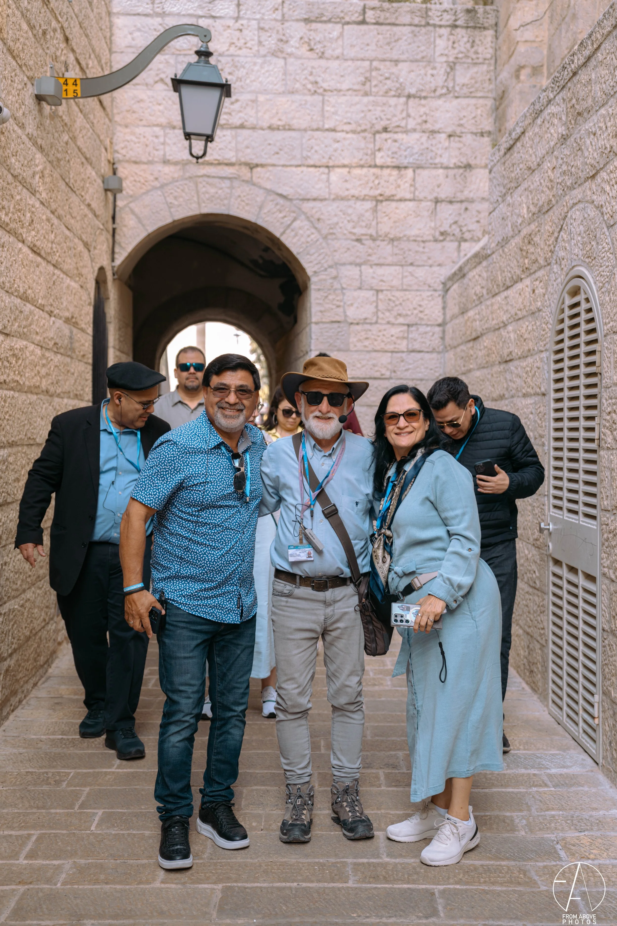 Group of tourists standing in an alleyway with stone walls, archway, and vintage street lamp.