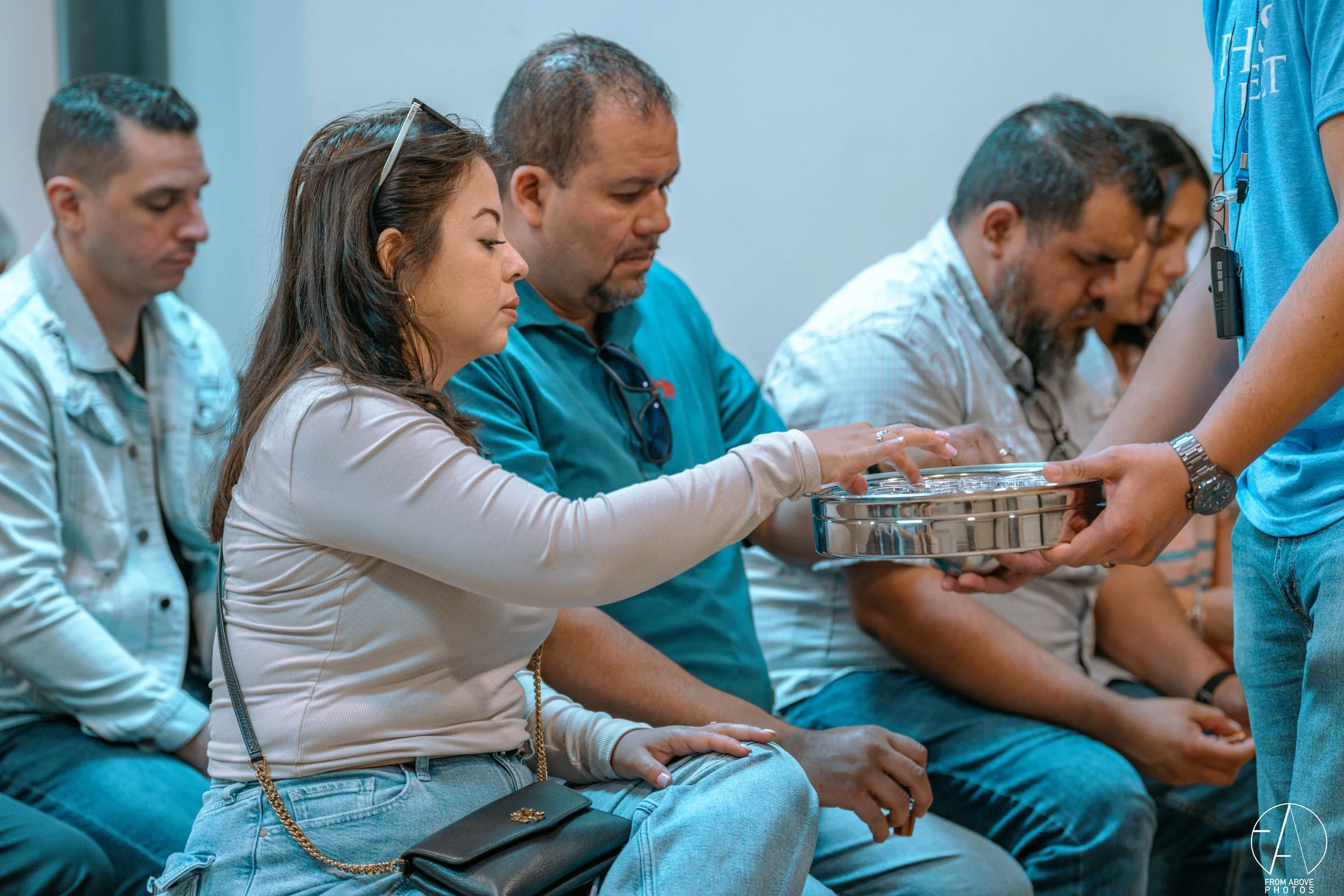People sitting in a line, receiving a silver tray from a person standing in front of them.