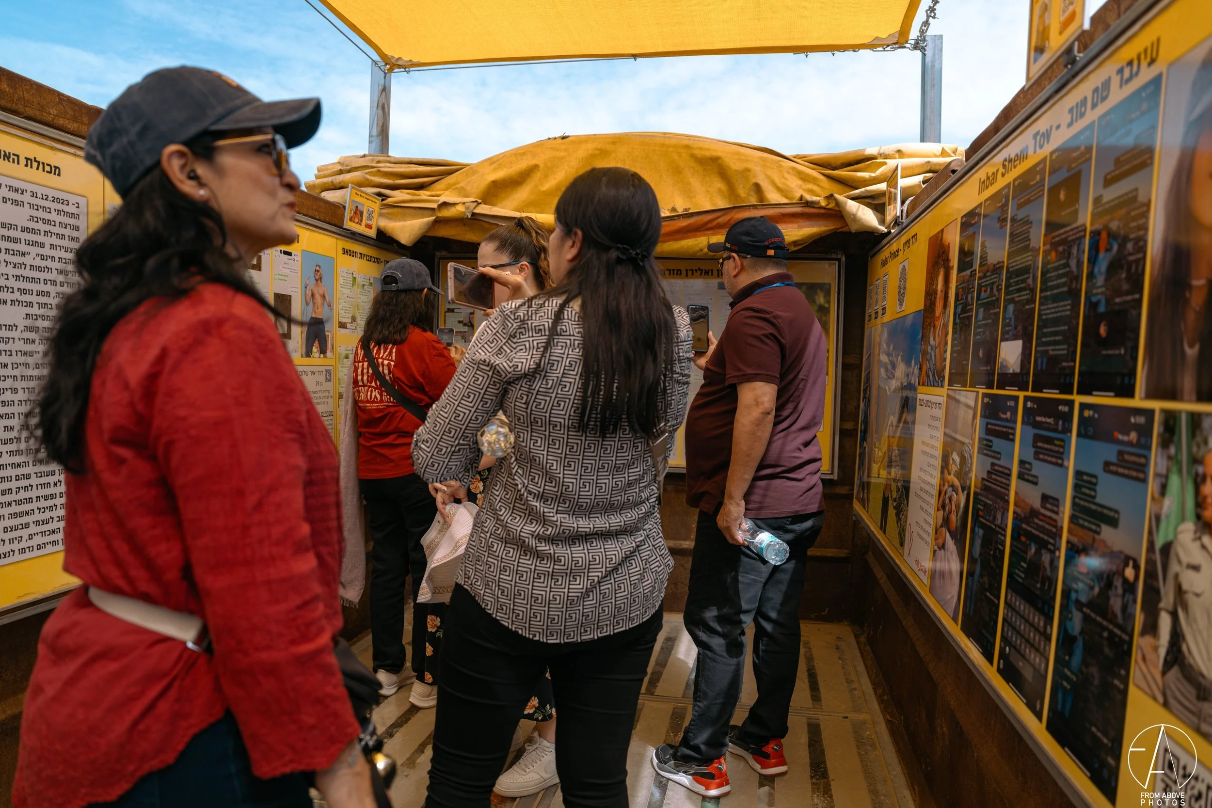People gathering and looking at informational posters at an outdoor booth under a yellow canopy.