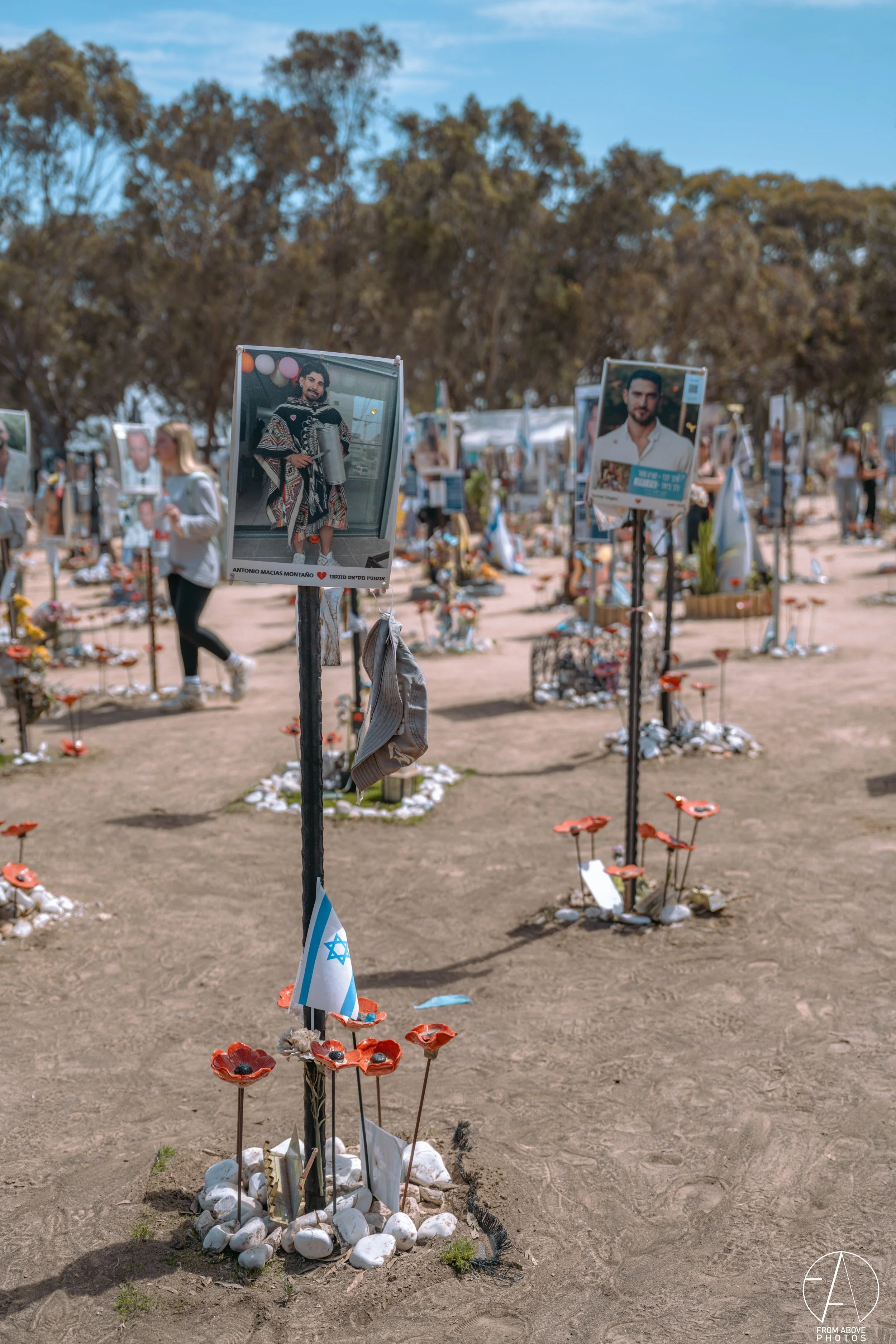 Memorial site with photographs of loved ones, small flags, and decorative flowers, likely a tribute or remembrance event.