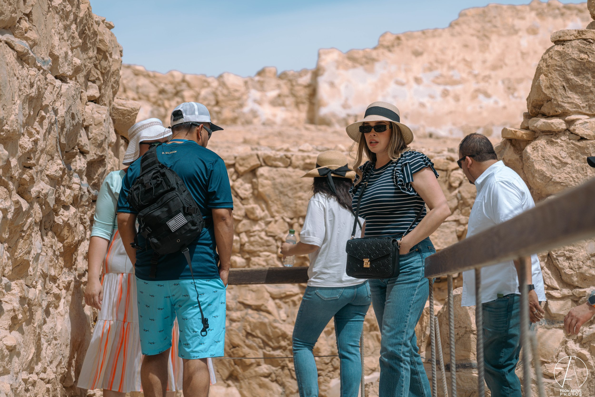 Tourists sightseeing at an archaeological site with stone walls and clear blue sky.
