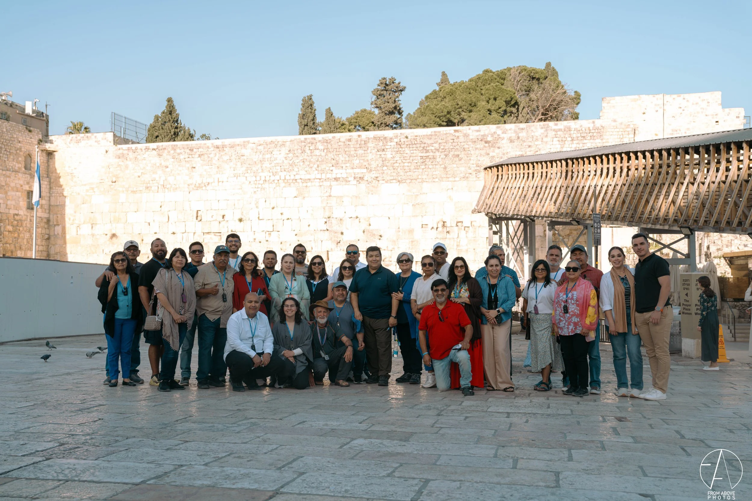 Group of diverse people posing for a photo at the historic Western Wall in Jerusalem, Israel, during daytime.