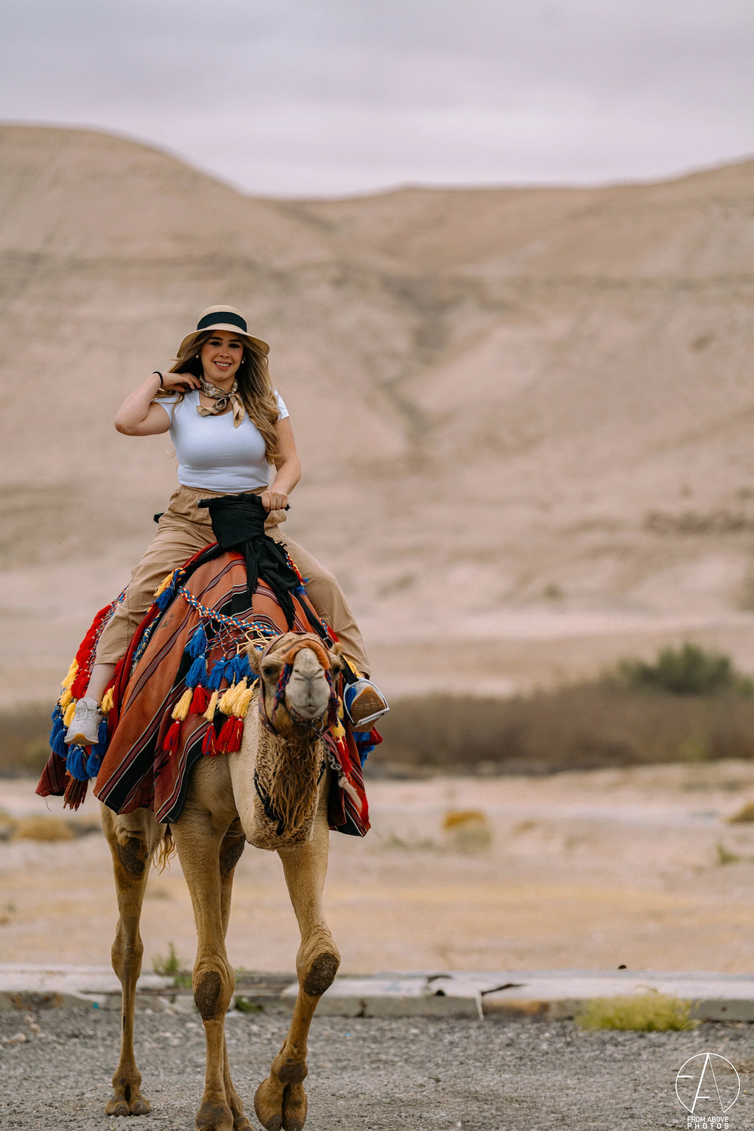 A woman riding a decorated camel in a desert landscape.