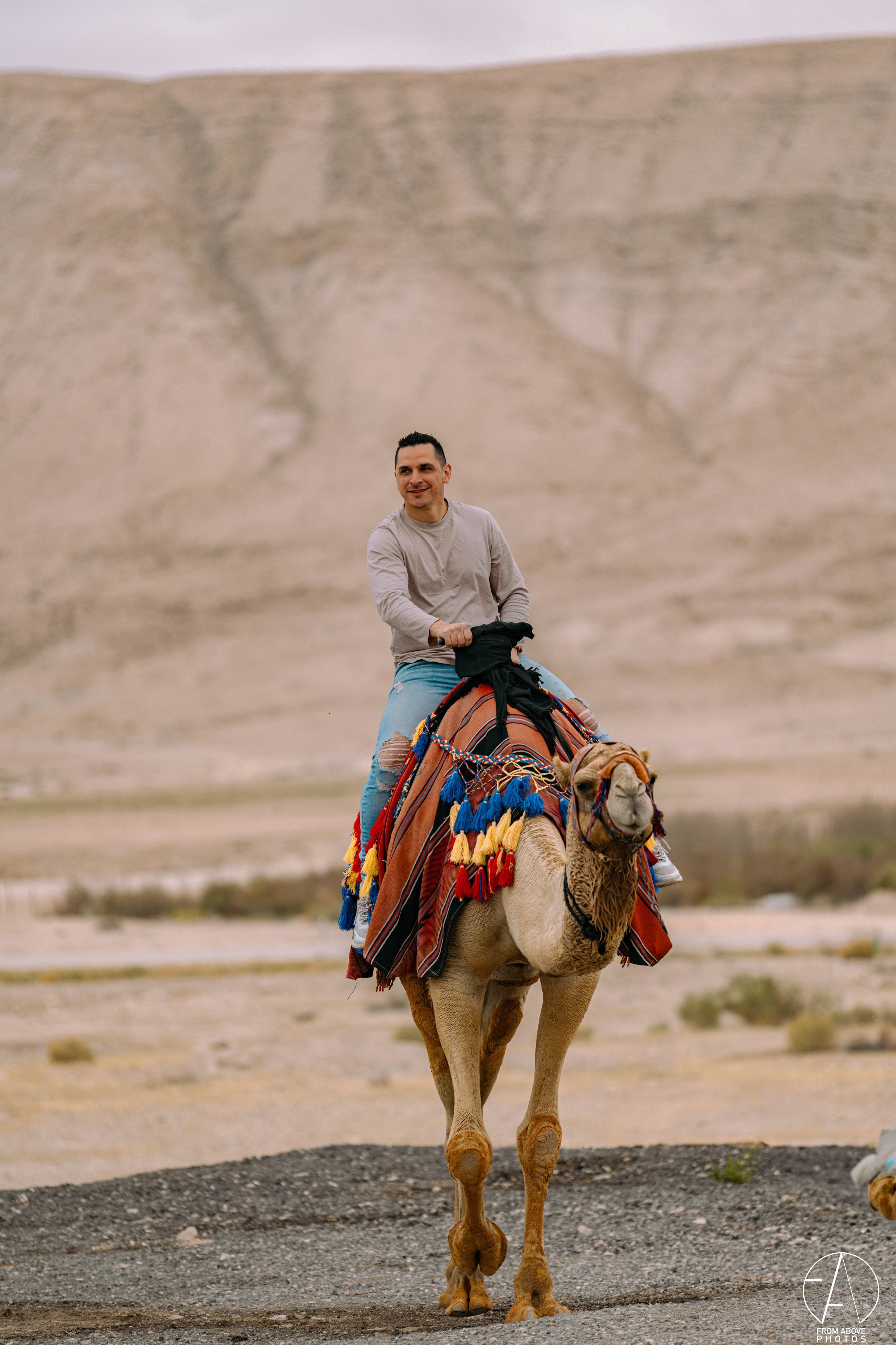 A man riding a camel in a desert landscape with distant hills in the background.