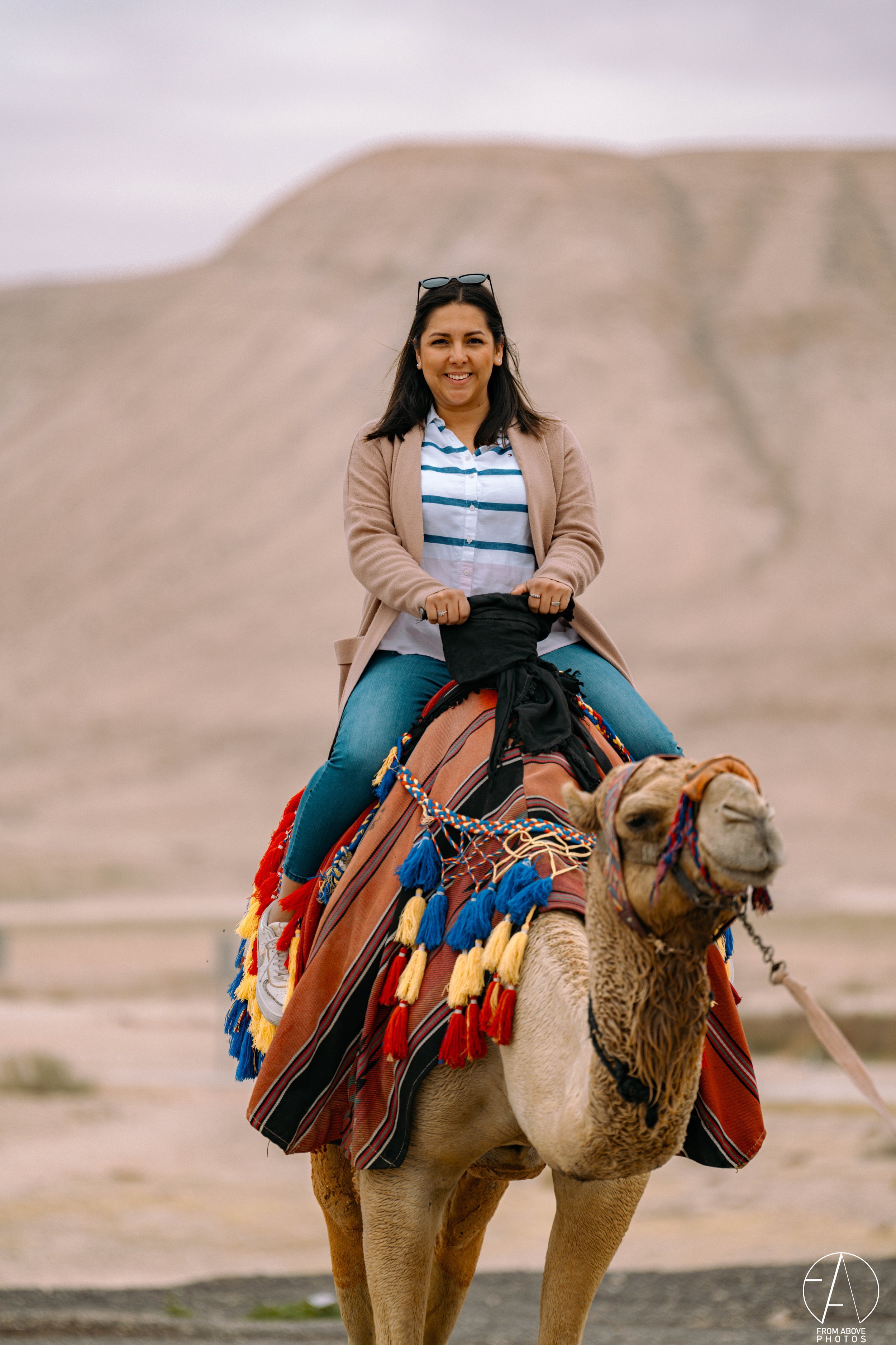 Woman riding a camel in a desert landscape with sandy hills in the background.