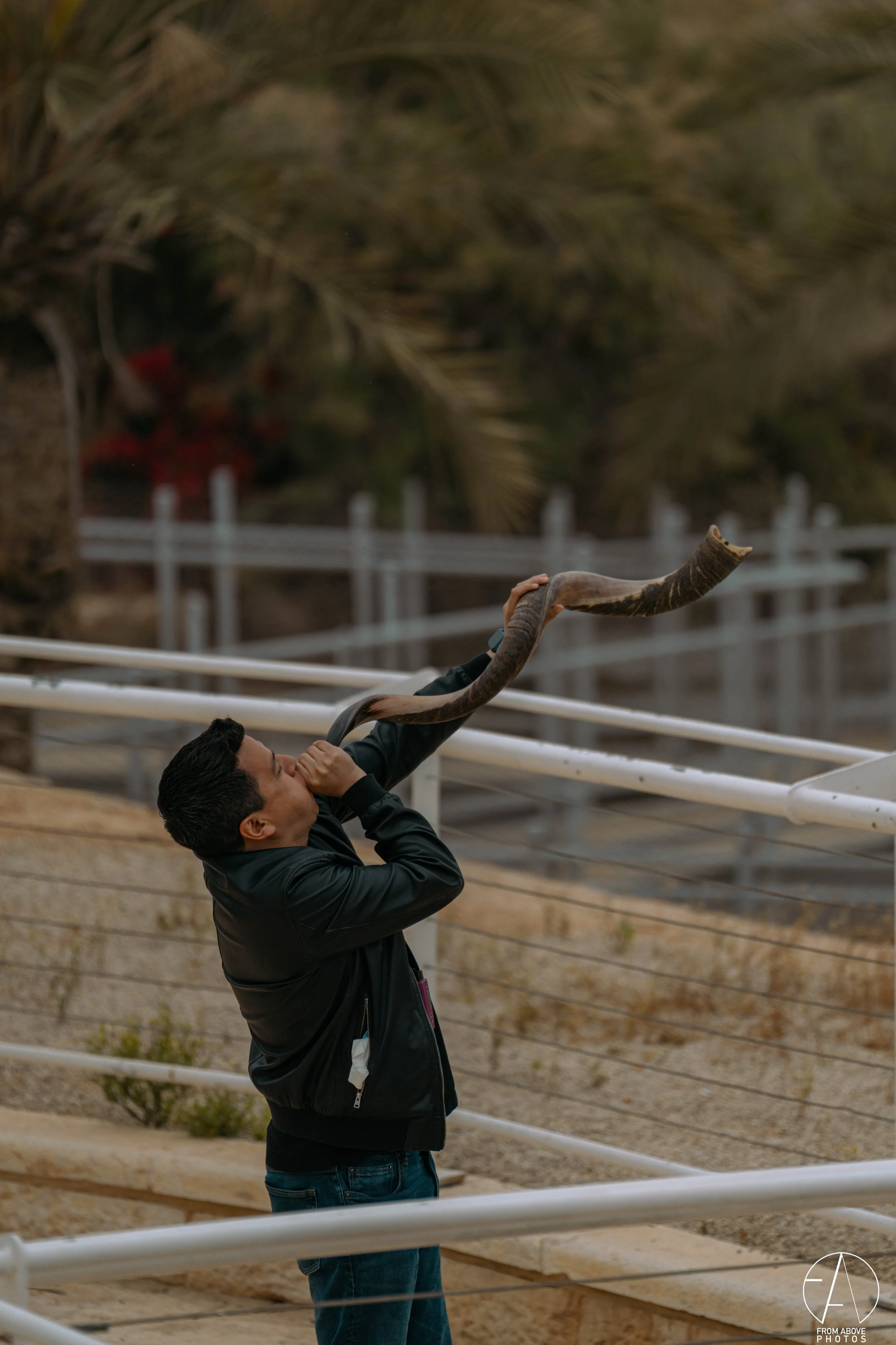 A man holding a snake to his face outdoors near white railings with trees in the background.