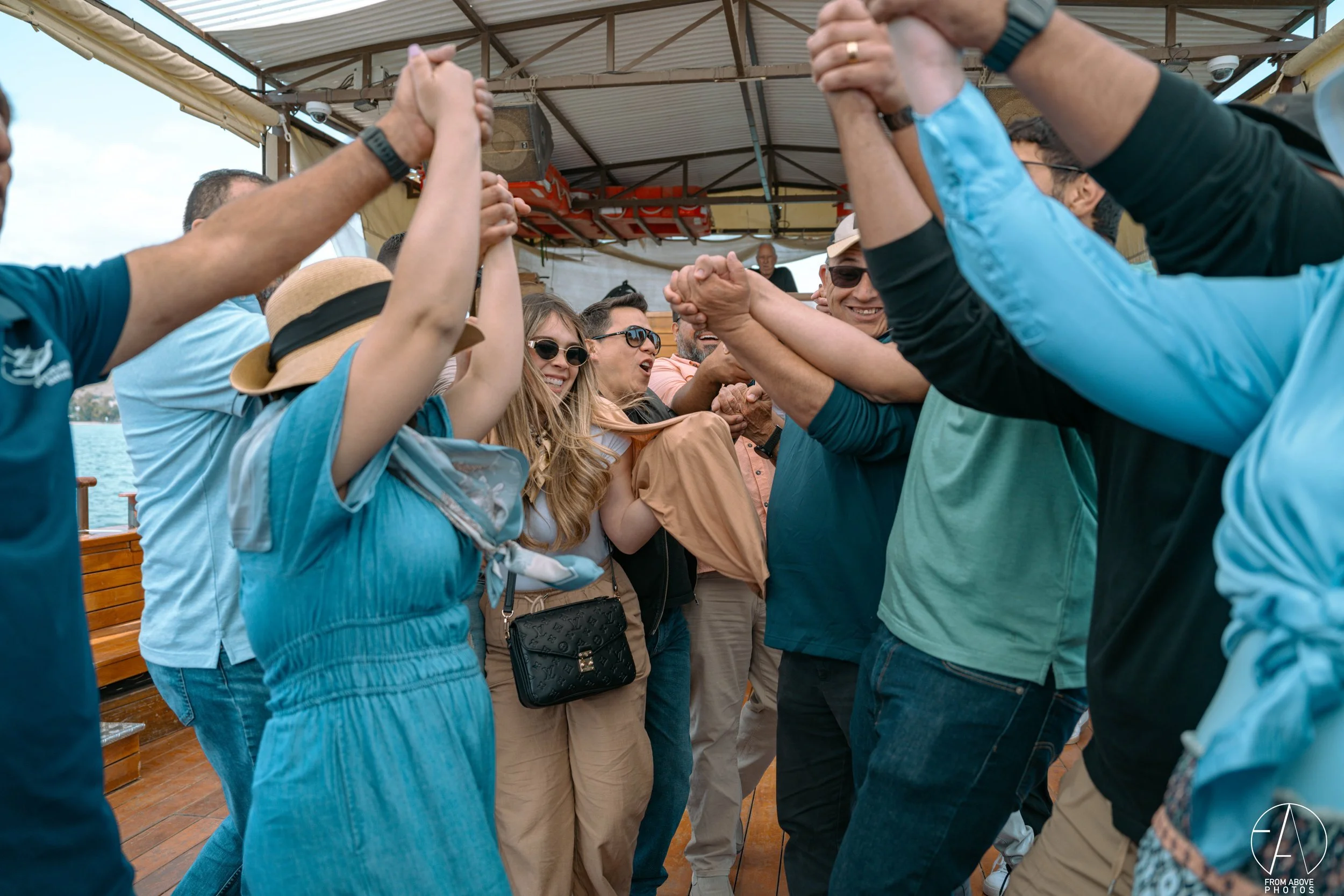 People holding hands in a circle on a boat deck, smiling and enjoying a moment together.