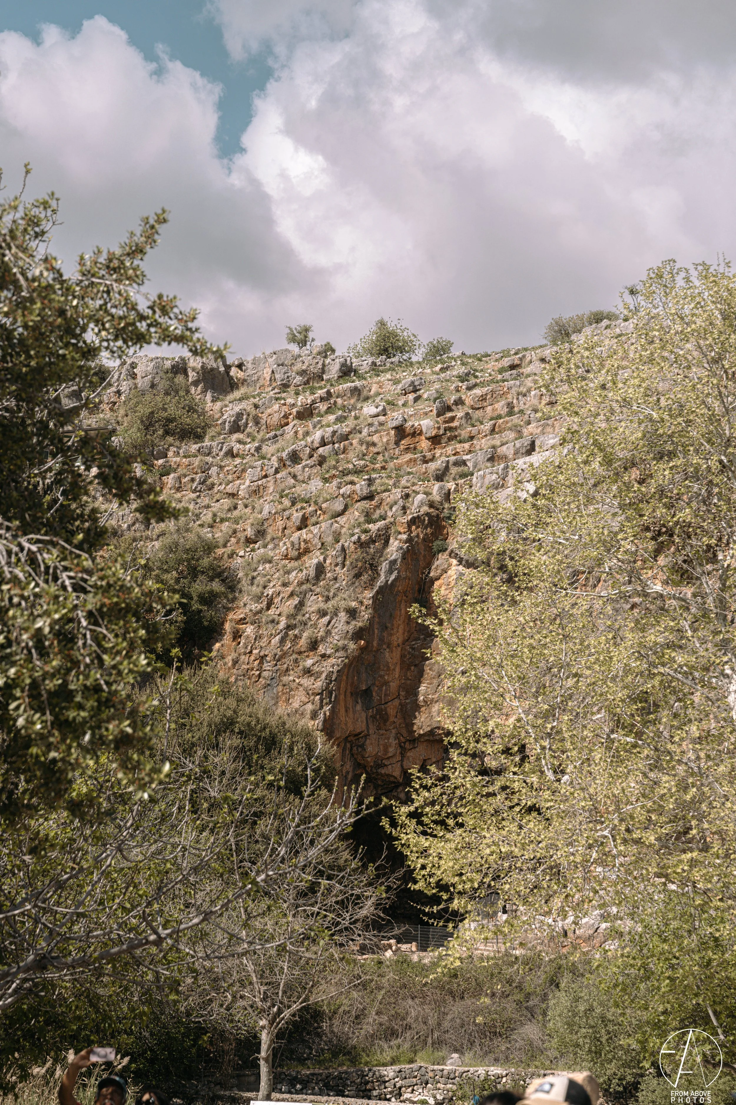 A rocky cliff with stairs built into it, surrounded by trees and a cloudy sky.