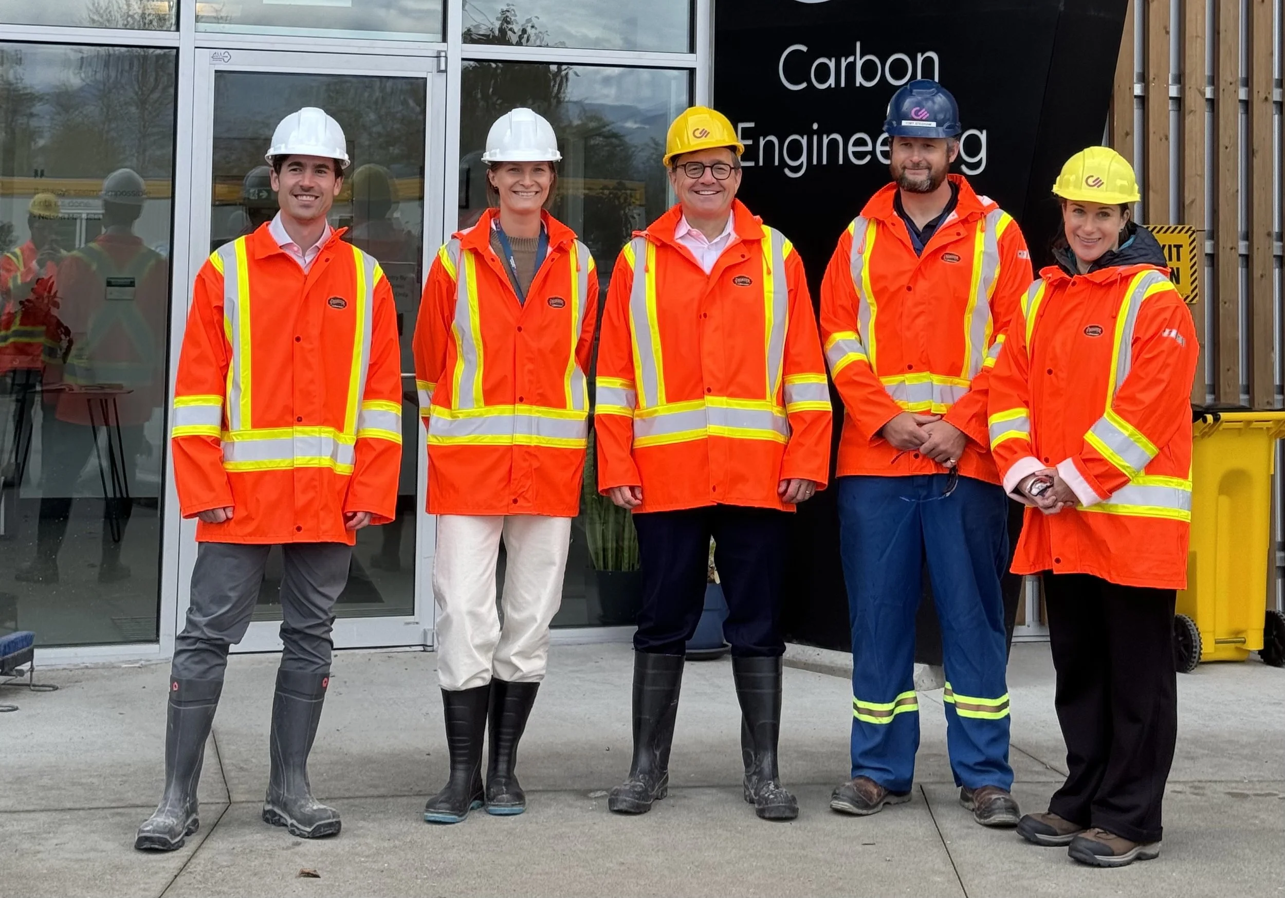 Group of five people wearing safety gear standing outside in front of a building with a sign that reads 'Carbon Engineering'.