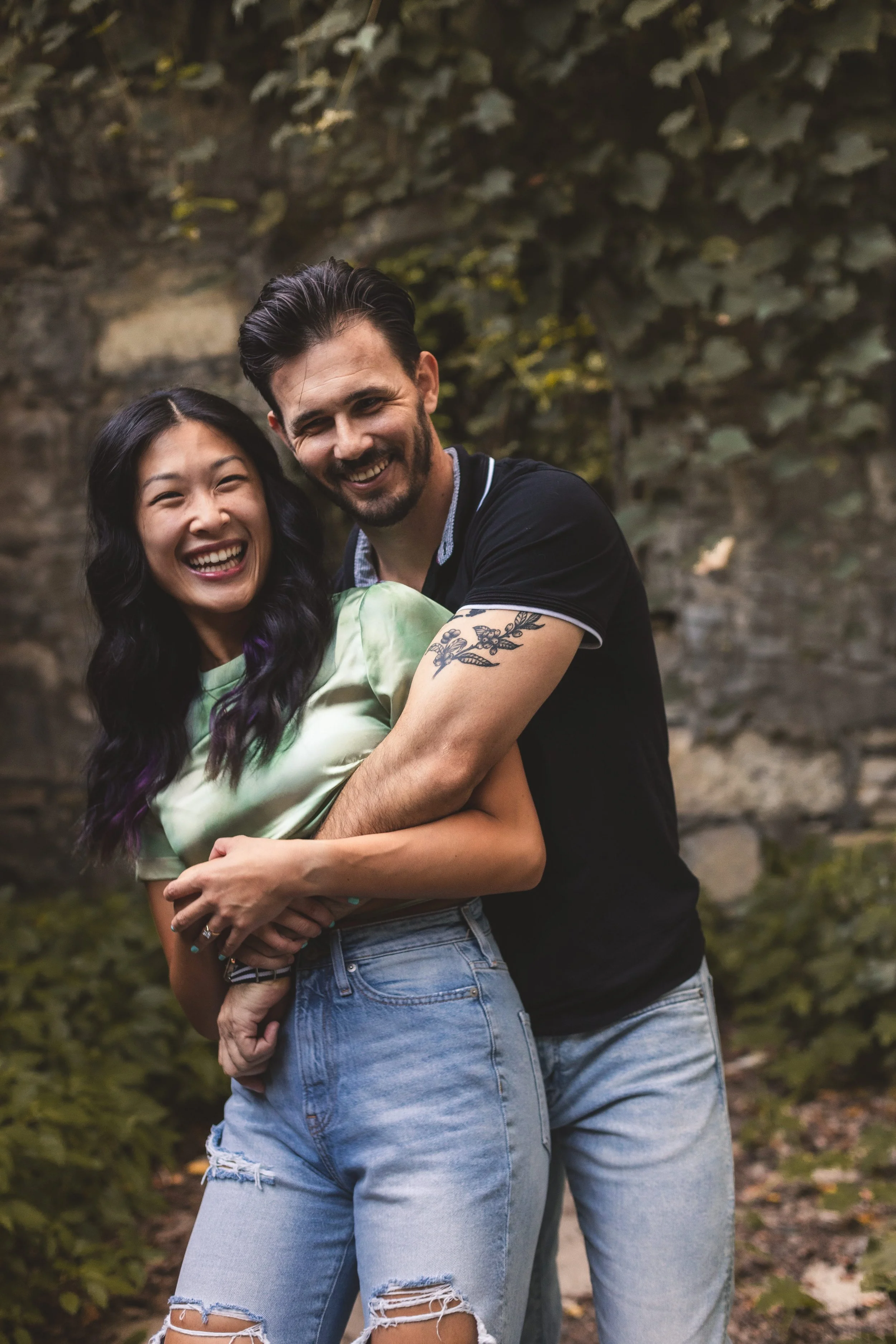 A happy couple embracing outdoors, with a stone wall and greenery in the background.