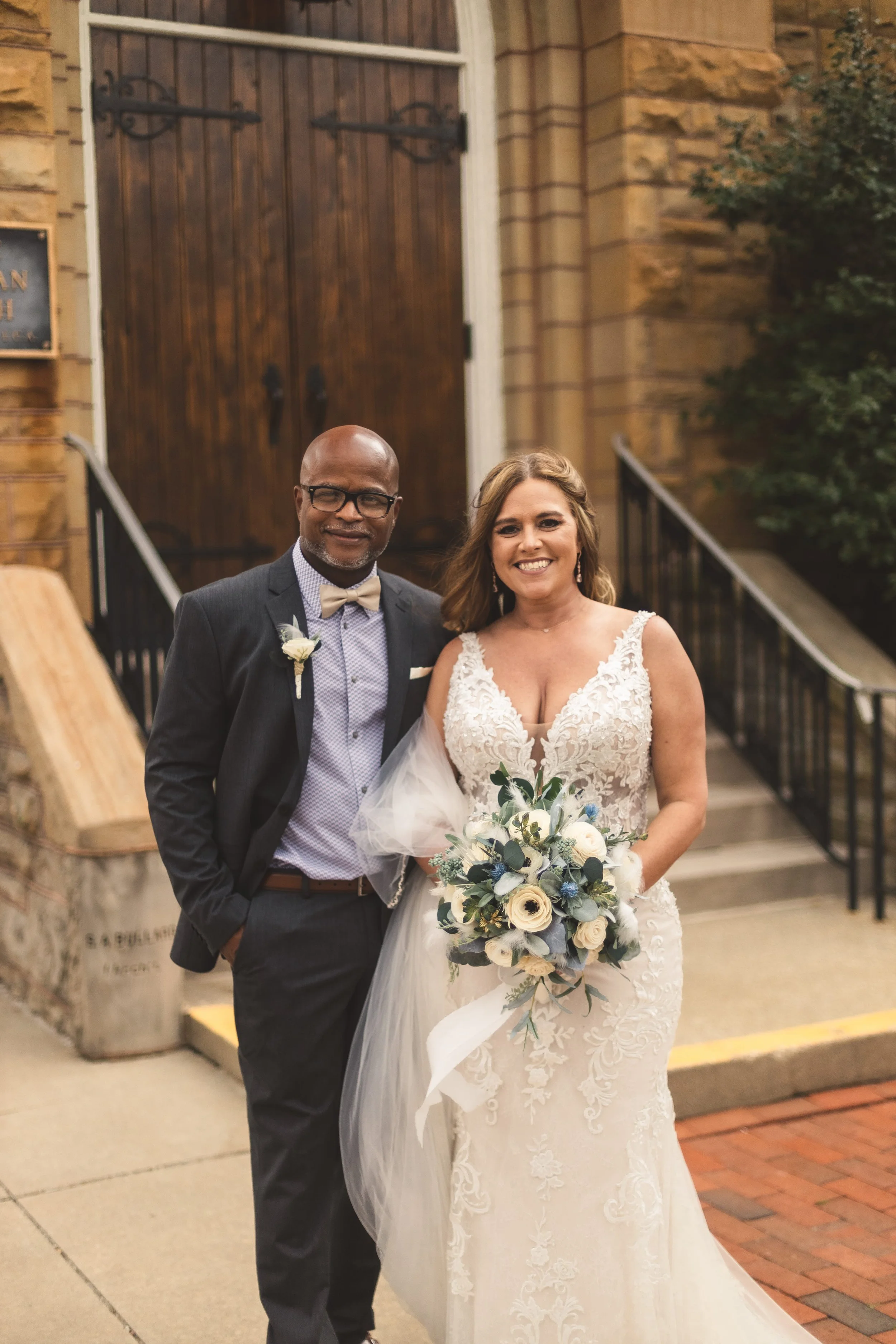 Bride and groom smiling together outside a stone church on their wedding day