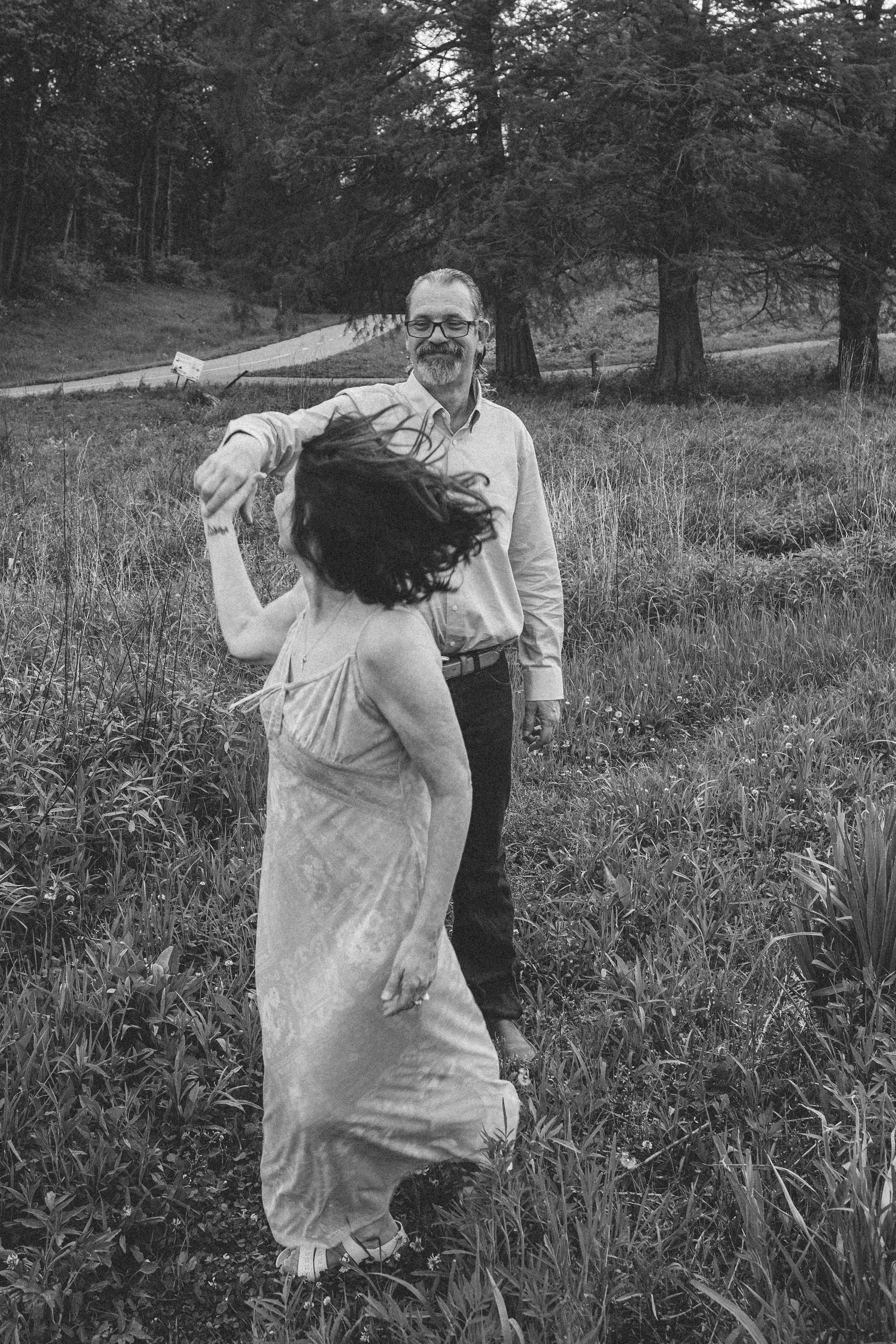 Black and white photo of couple spinning together in an open field during engagement session