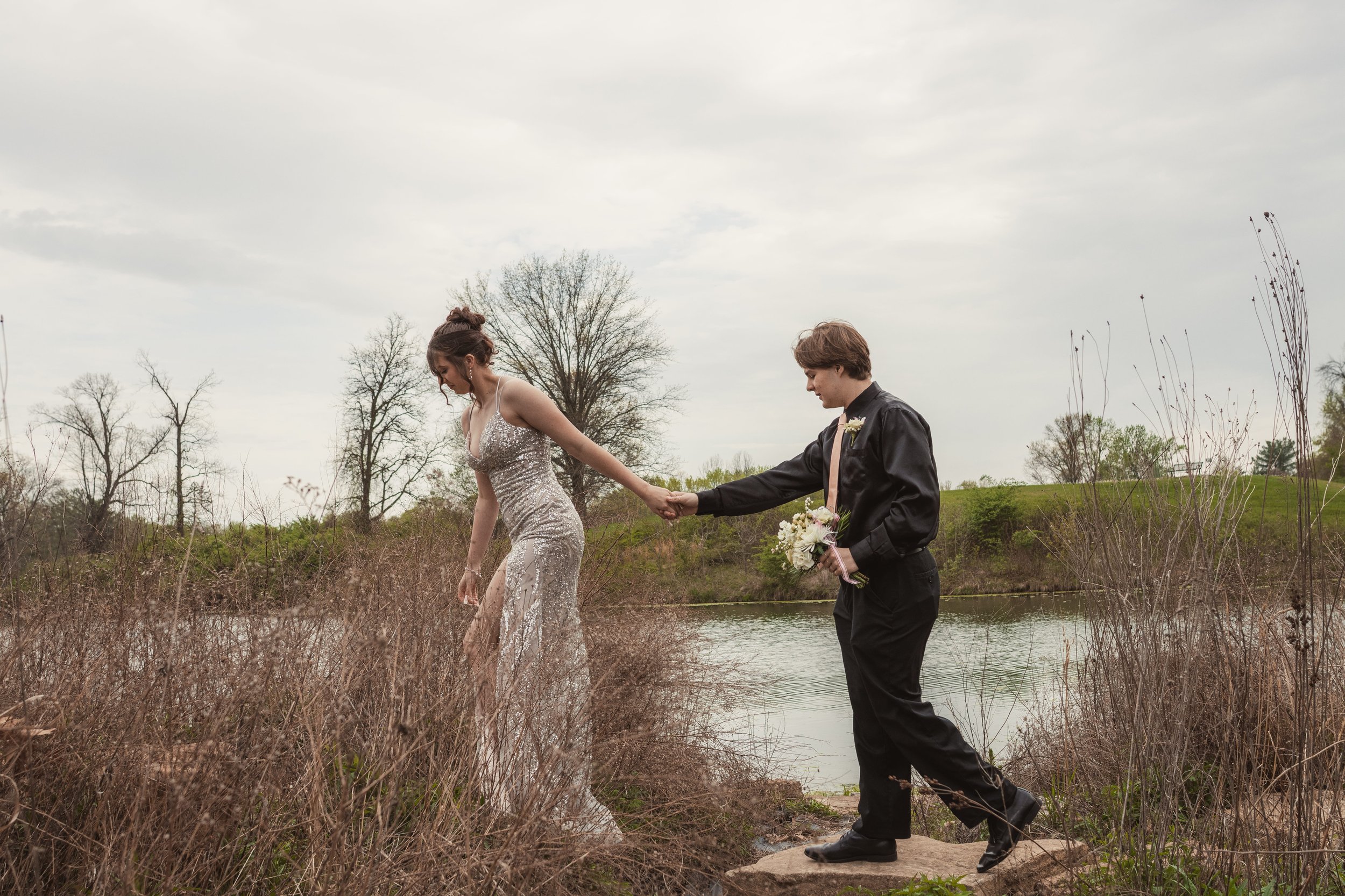 Young couple in formal attire standing near a lake with bare winter trees, prom portrait